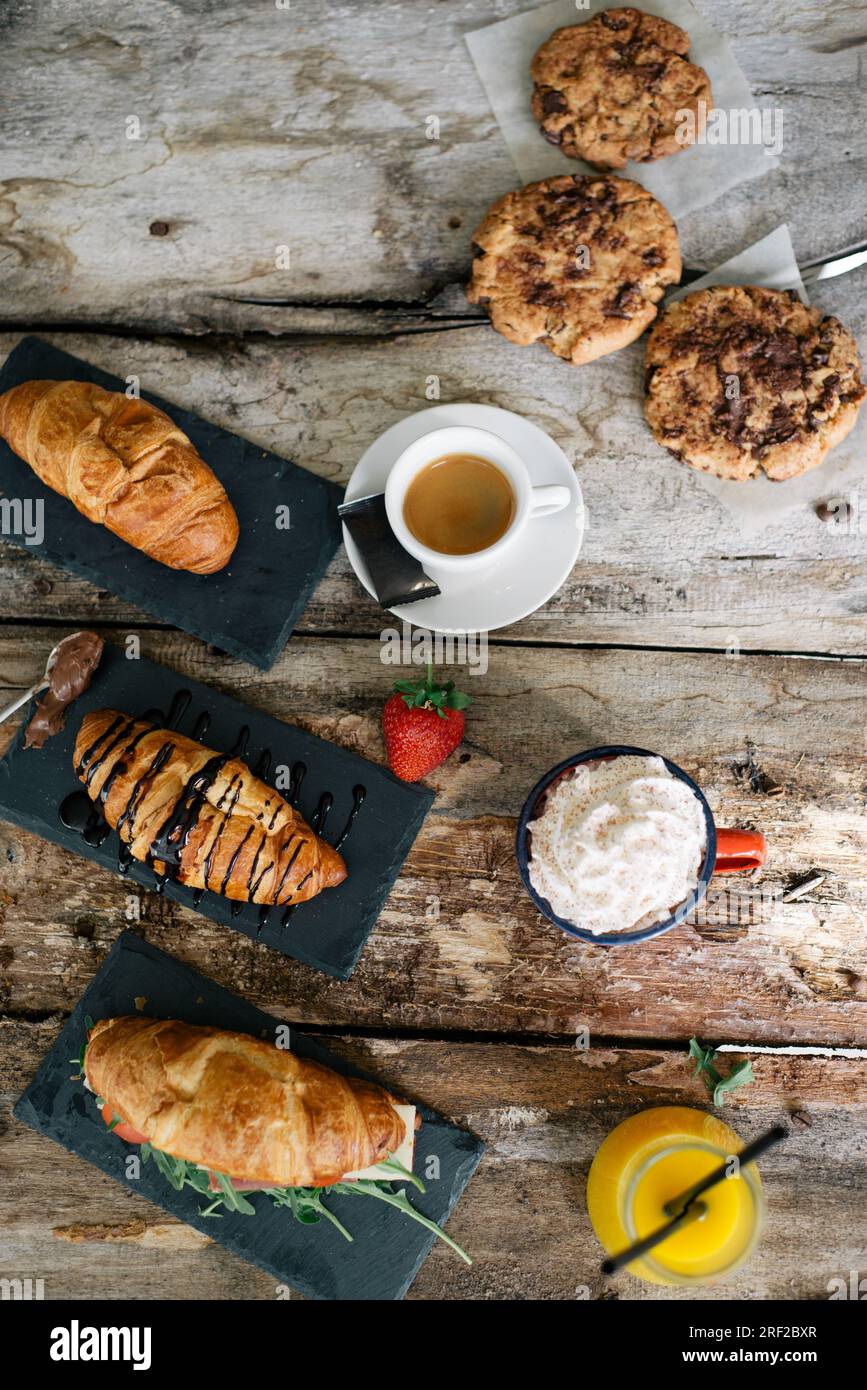 Croissant, caffè, torta, panna e fragole crude su un tavolo di legno. Foto Stock