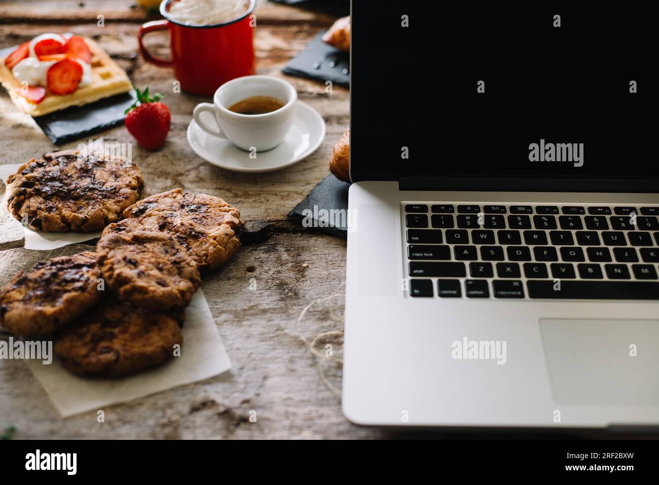 Croissant, caffè, torta, panna, fragola cruda e notebook Foto Stock