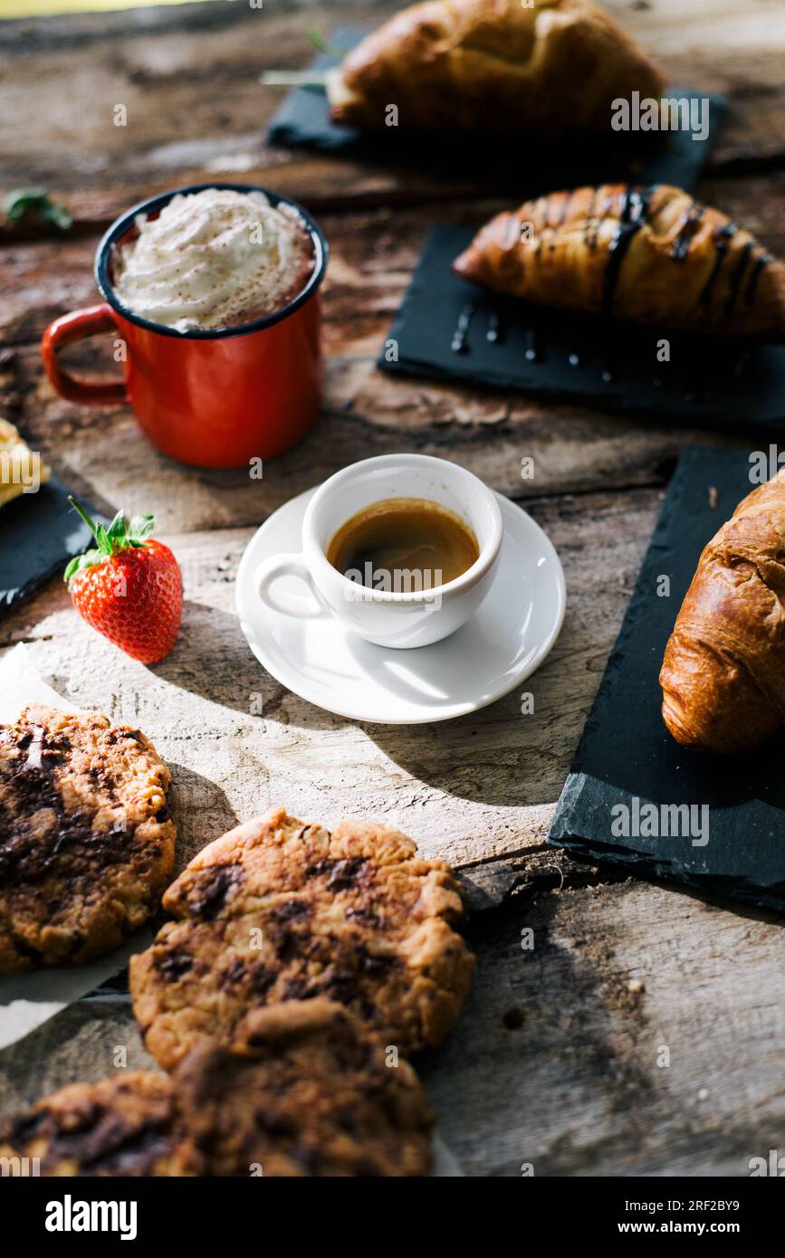 Croissant, caffè, torta, panna e fragole crude su un tavolo di legno. Foto Stock