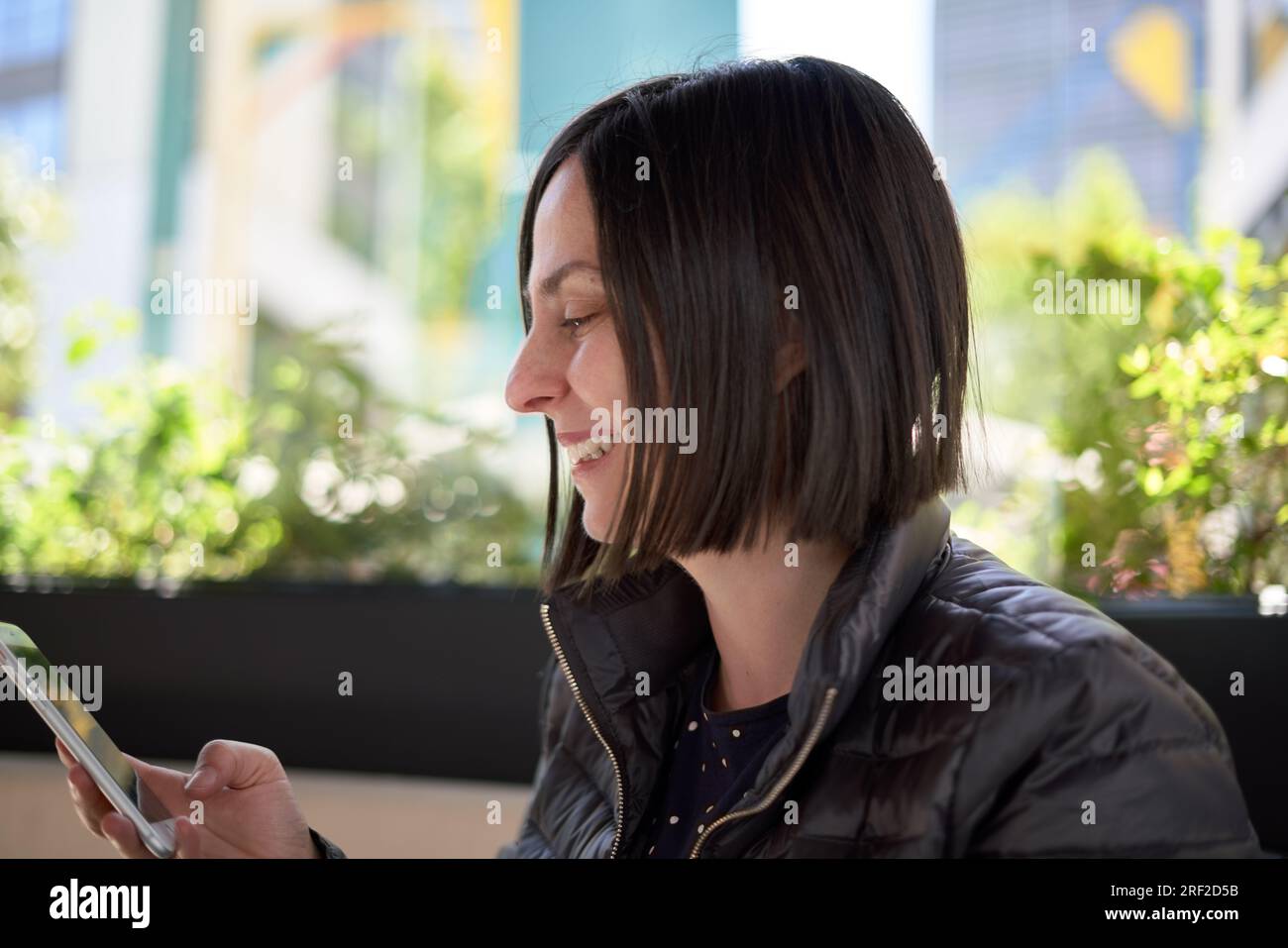 Donna che sorride e usa il suo cellulare Foto Stock