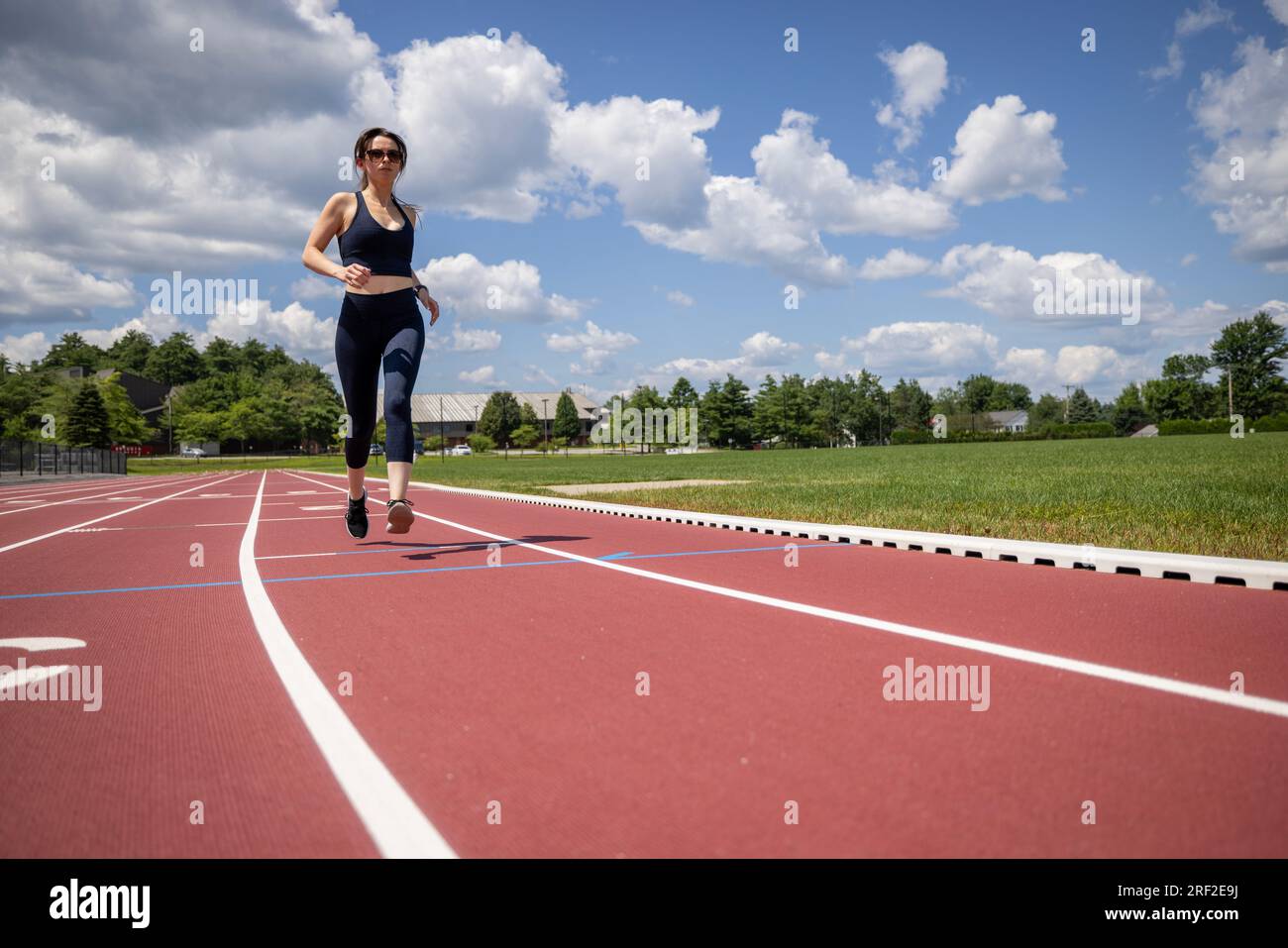 donna in forma con abiti da corsa neri che sfreccia su una pista Foto Stock