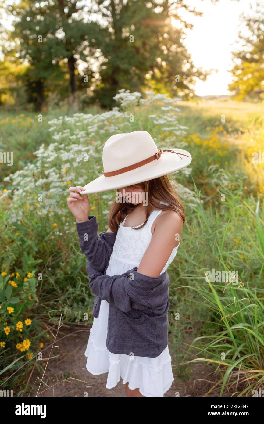 Bambina in abito bianco in piedi con fiori selvatici al tramonto Foto Stock
