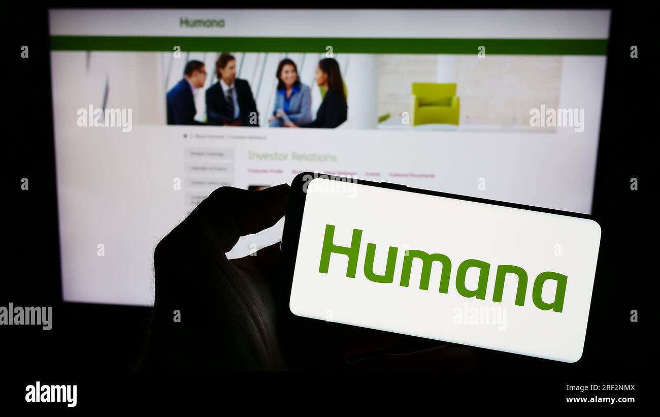 Persona in possesso di cellulare con logo della compagnia di assicurazione sanitaria statunitense Humana Inc. Sullo schermo di fronte alla pagina Web aziendale. Concentrarsi sul display del telefono. Foto Stock