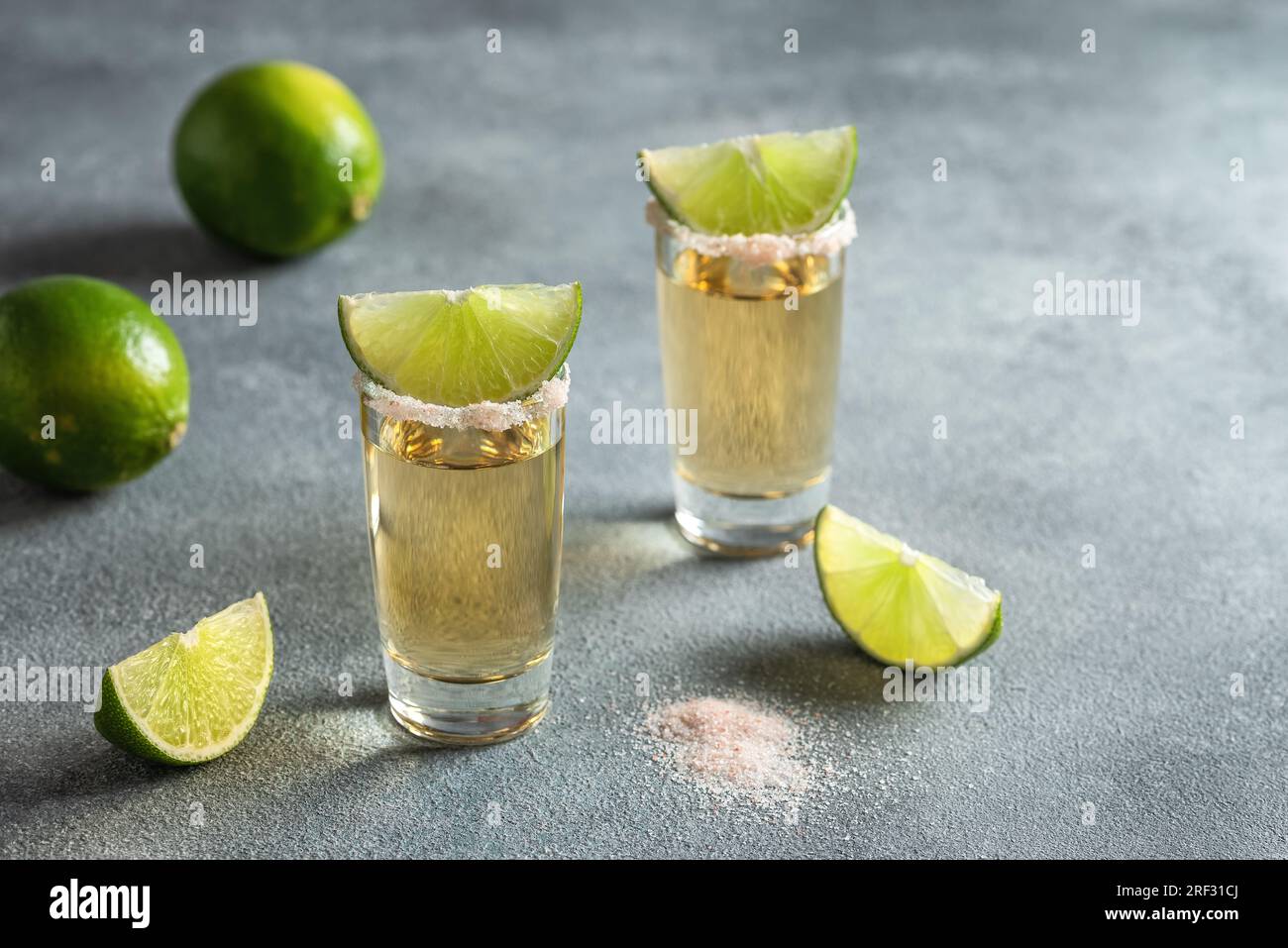 Due shot di tequila con lime e sale rosa, sfondo in pietra grigia. Vista laterale, messa a fuoco selettiva, spazio di copia. Foto Stock