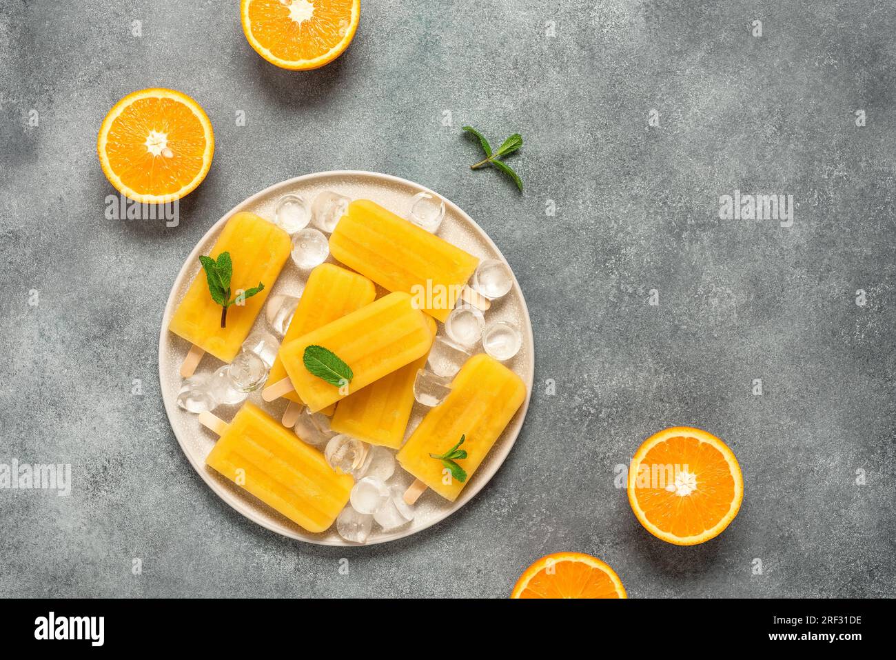 Ghiaccioli arancioni, sfondo grigio. Vista dall'alto, disposizione piatta, spazio copia, verticale. Dessert rinfrescante estivo. Succo d'arancia congelato su un bastoncino. Foto Stock