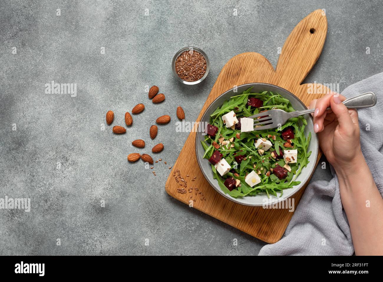 Donna che mangia insalata sana. Ciotola con insalata di barbabietole con rucola e feta. Sfondo grigio cemento. Vista dall'alto, base piatta. Foto Stock