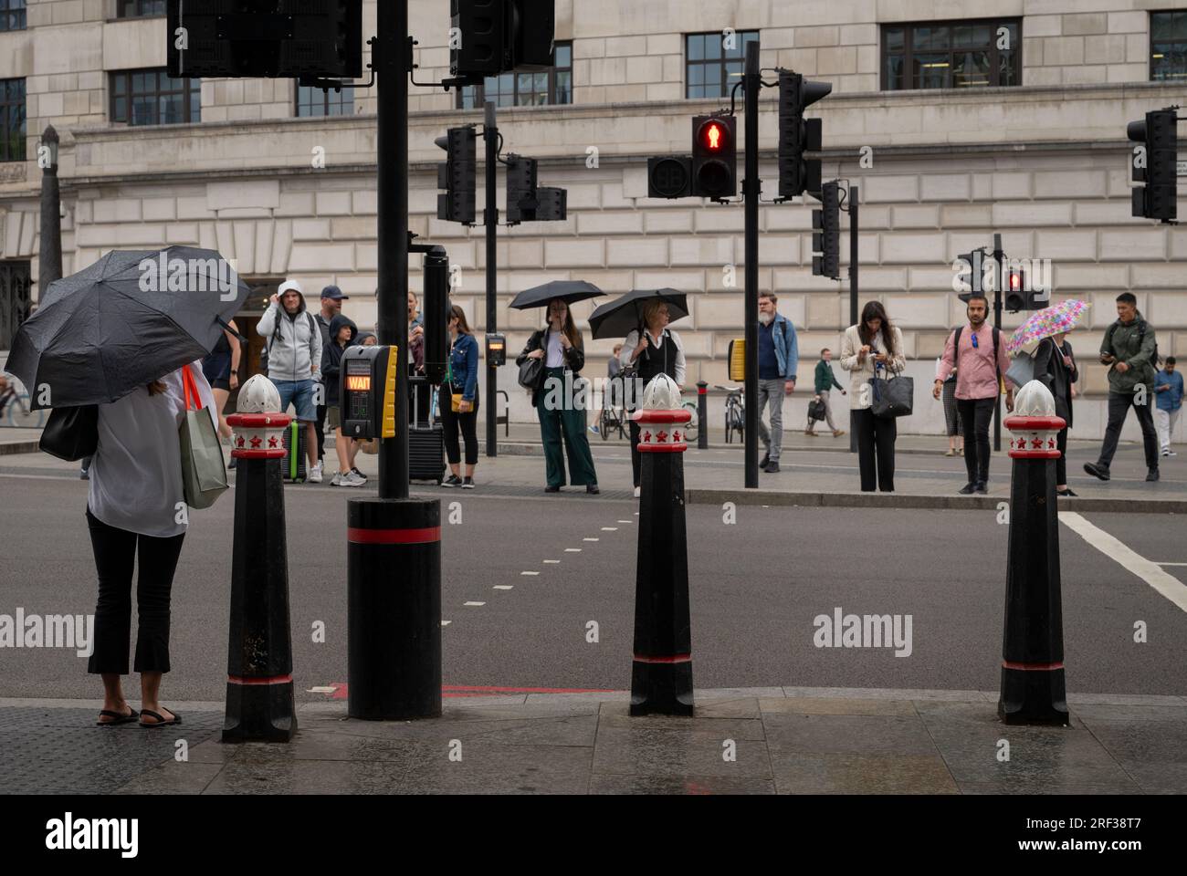 Londra, Regno Unito: Persone in attesa di attraversare la strada in un passaggio pedonale sotto la pioggia. Victoria Embankment vicino alla stazione di Blackfriars nella City di Londra. Foto Stock