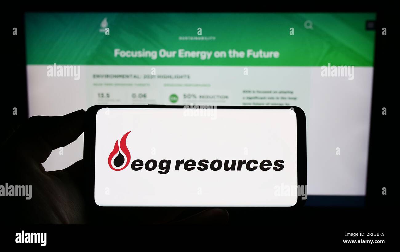 Persona che possiede il cellulare con il logo della società energetica statunitense EOG Resources Inc. Sullo schermo davanti alla pagina Web aziendale. Concentrarsi sul display del telefono. Foto Stock