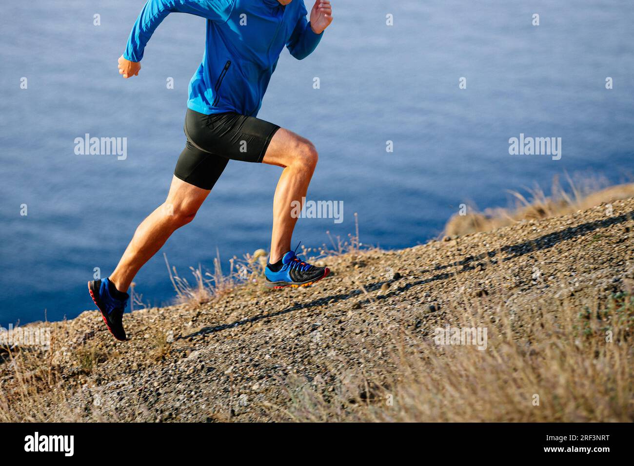l'atleta runner inizia a correre in montagna in salita con giacca blu e tights neri, sfondo di mare Foto Stock