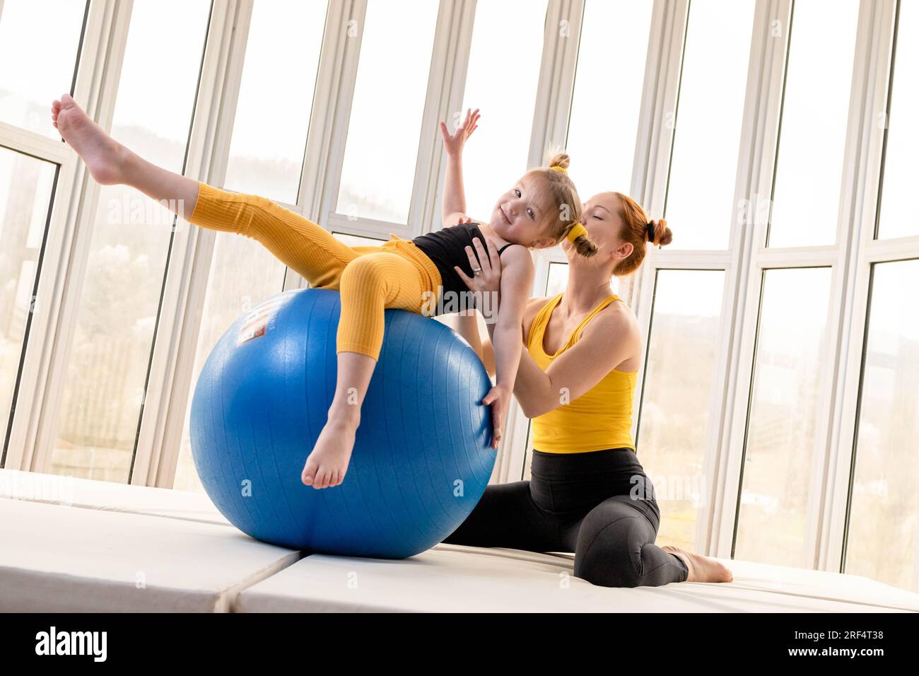 Mamma e figlia giovani si divertono con la palla fitness in palestra Foto Stock