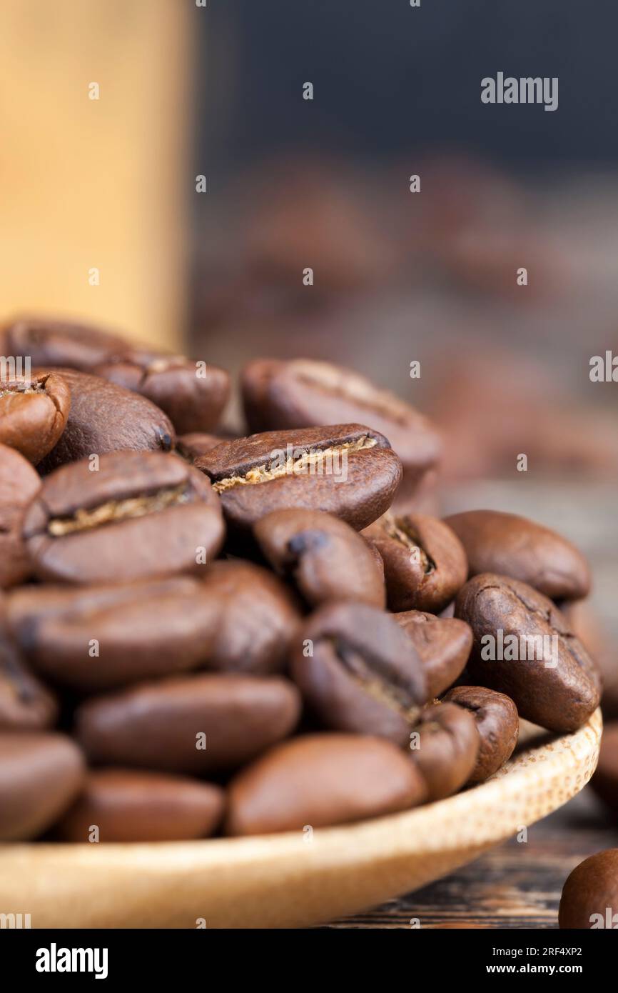chicchi di caffè aromatici in un cucchiaio di legno, chicchi di caffè per la produzione di delizioso caffè in un misurino a base di bambù, chicchi di caffè in balena Foto Stock