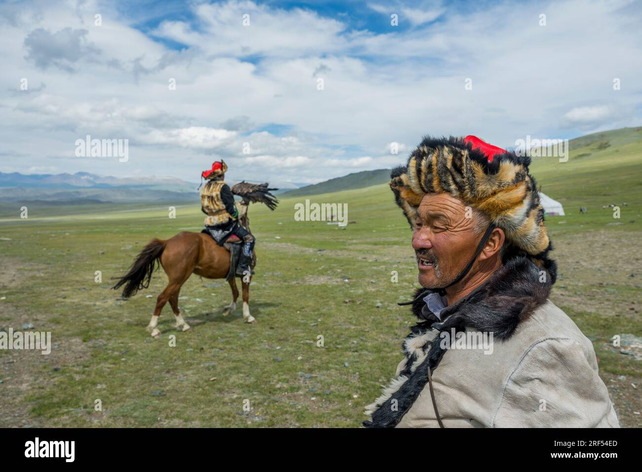 Il cacciatore di aquile kazako Dalaikhan (in primo piano) e suo figlio a cavallo con in mano un'aquila reale nel suo campo estivo in una remota valle nell'Altai Moun Foto Stock
