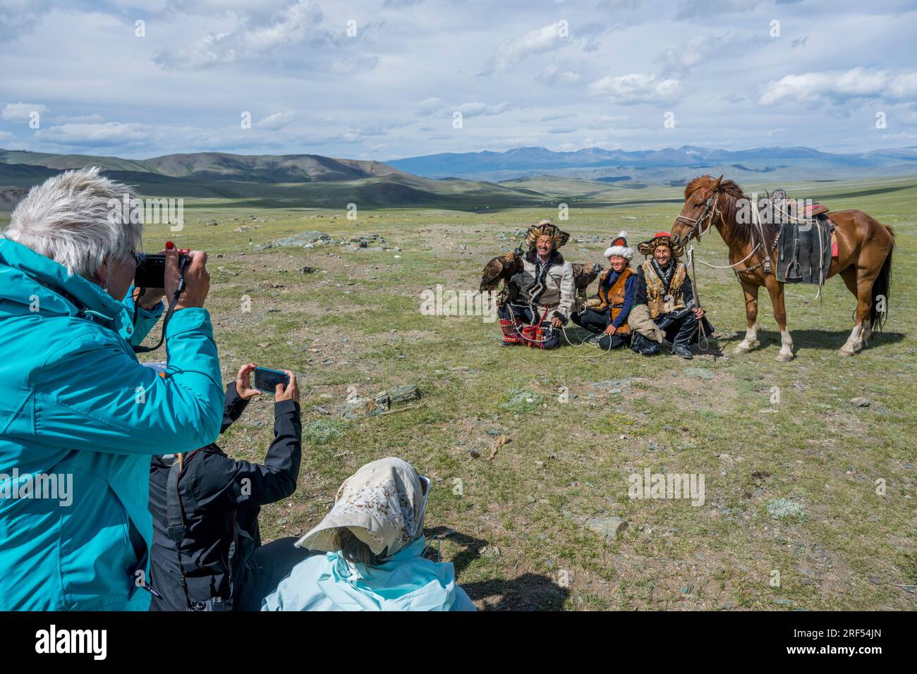 I turisti che fotografano una famiglia kazaka di cacciatori di aquile con aquile d'oro al campo estivo in una valle remota nelle montagne Altai (montagne Altay) Foto Stock