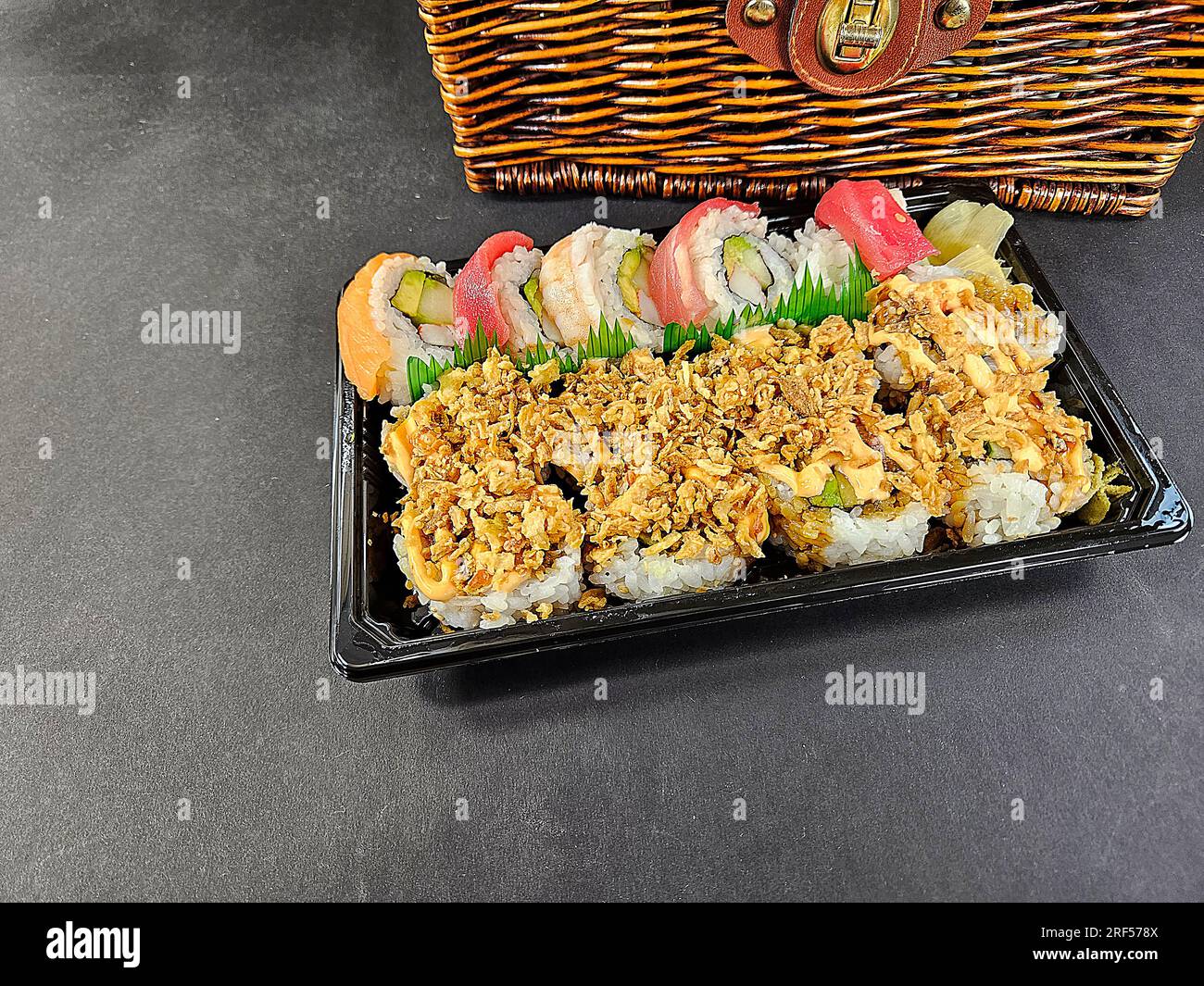 Involtini di sushi freschi su un vassoio di plastica nera con cestino di vimini marrone Foto Stock