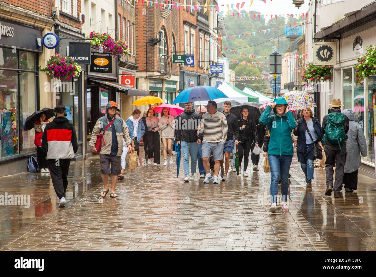 Persone che camminano e fanno shopping sotto la pioggia, sotto gli ombrelli nella strada principale di Winchester, durante il terribile clima estivo piovoso in Inghilterra del 2023 Foto Stock