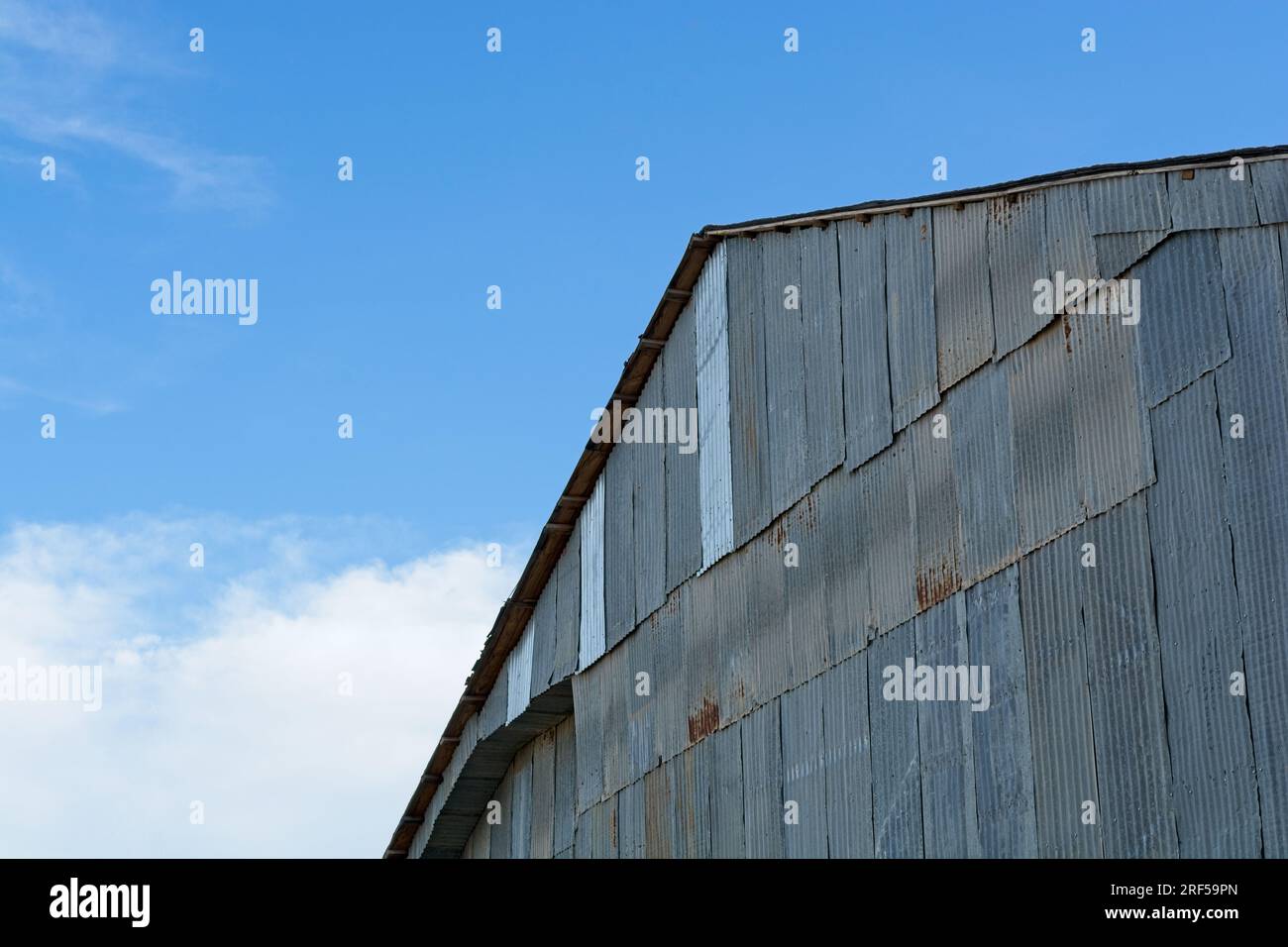 Stalla resistente agli agenti atmosferici con rivestimento in lamiera di metallo ondulato fissato contro il cielo blu Foto Stock