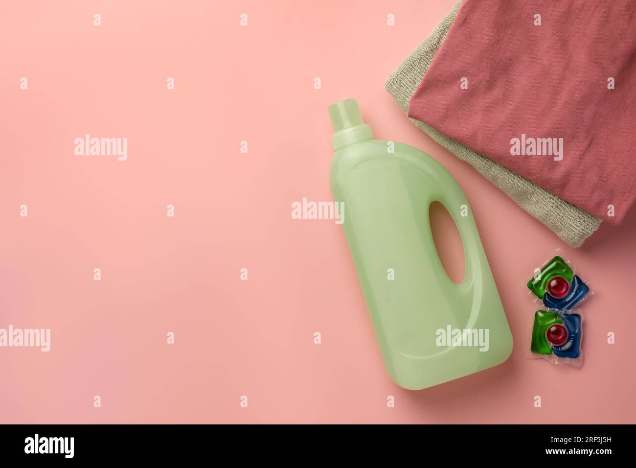 Bottiglia di addolcitore per tessuti, abiti puliti impilati e capsule per bucato su sfondo rosa, spianata. Spazio per il testo Foto Stock