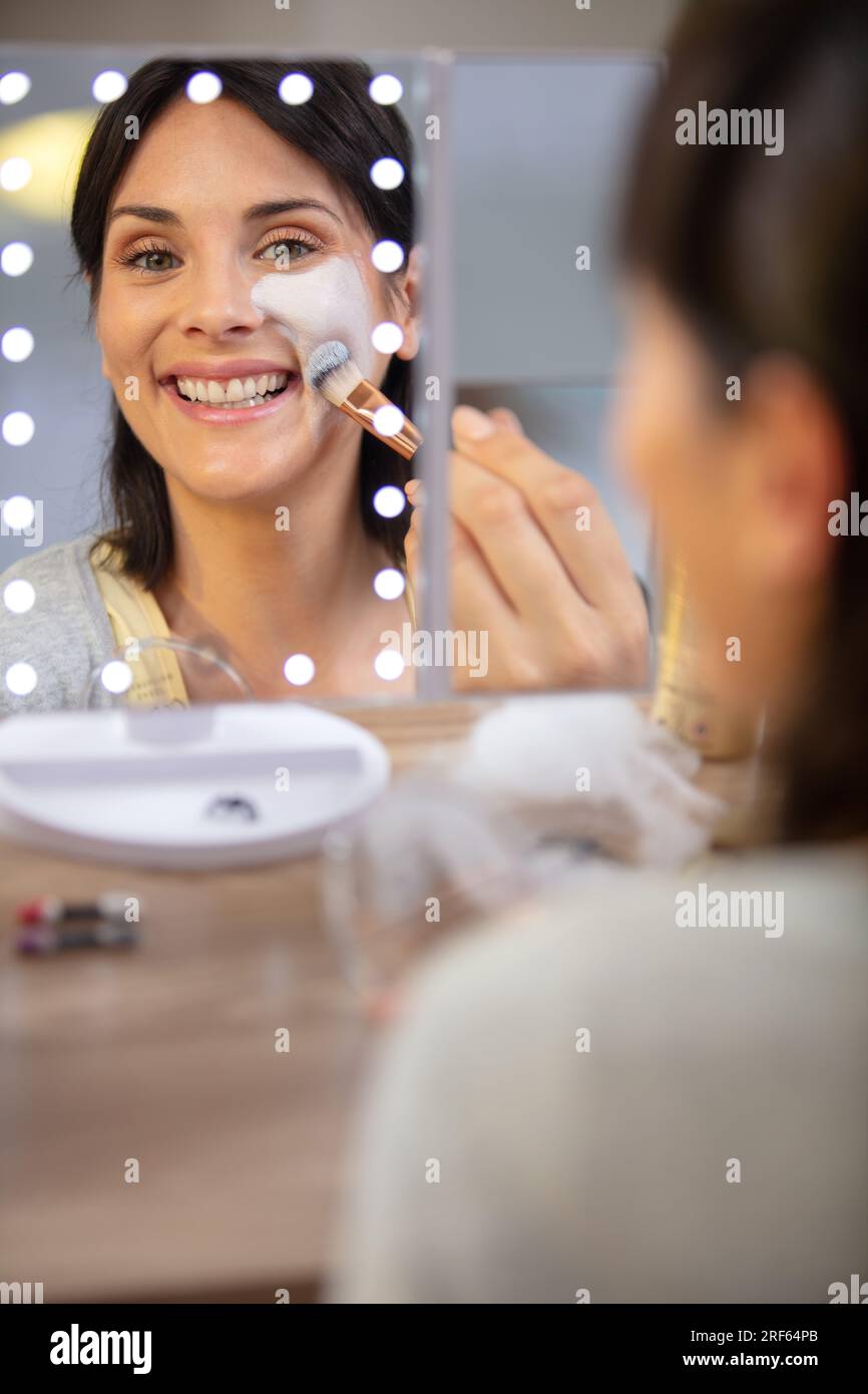 riflesso di una donna che applica la vernice del viso nello specchio illuminato Foto Stock