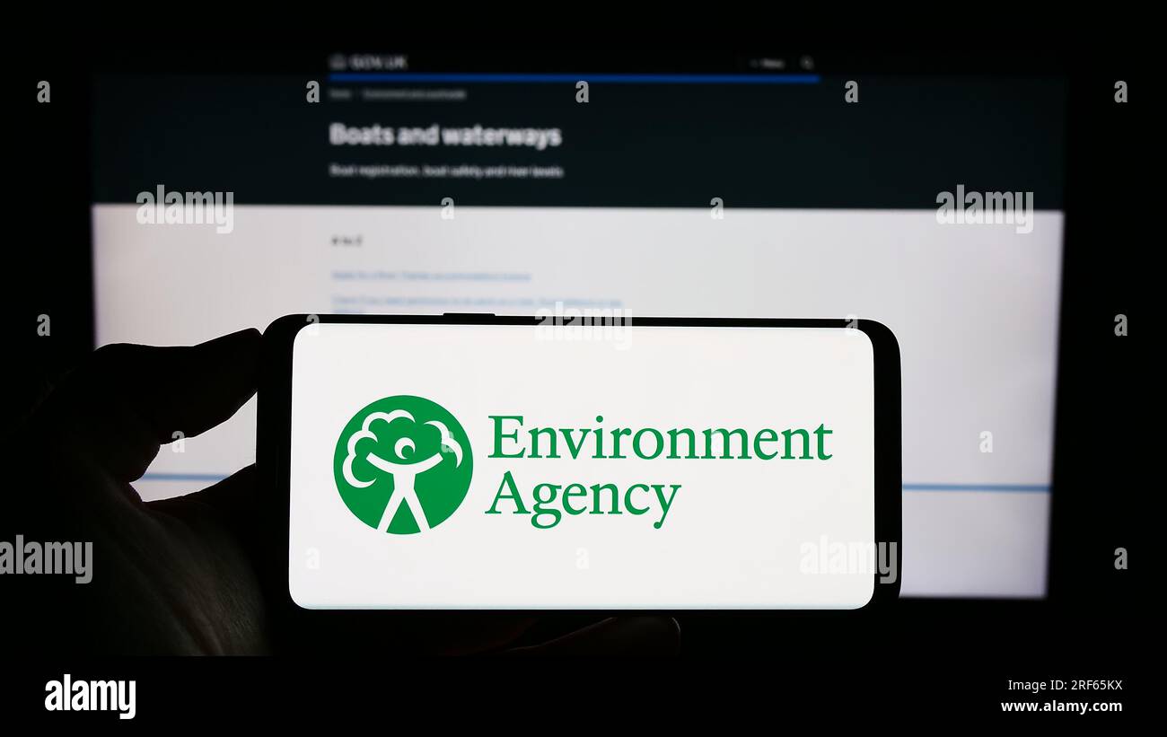Persona in possesso di un cellulare con il logo della British Public Body Environment Agency (EA) sullo schermo davanti alla pagina Web. Concentrarsi sul display del telefono. Foto Stock