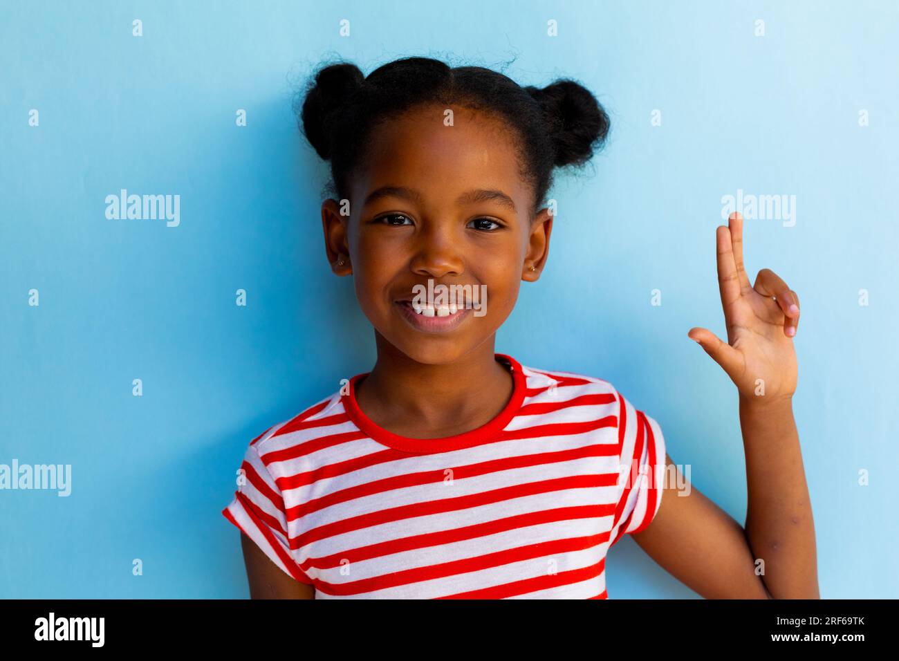 Felice studentessa afroamericana che fa linguaggio dei segni con mano su sfondo blu Foto Stock