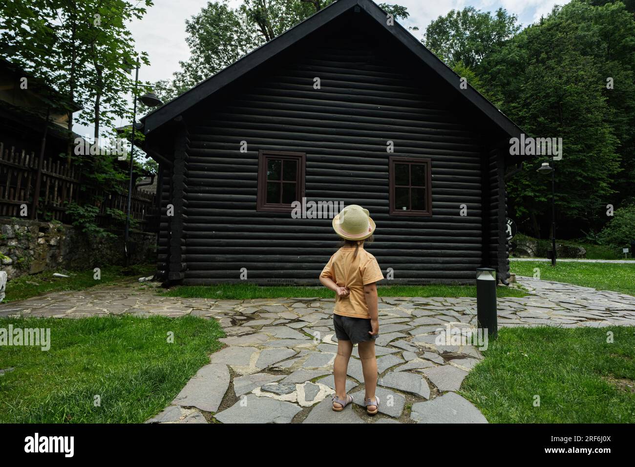 La ragazza con un cappello si trova vicino a una casa di legno nel parco. Foto Stock