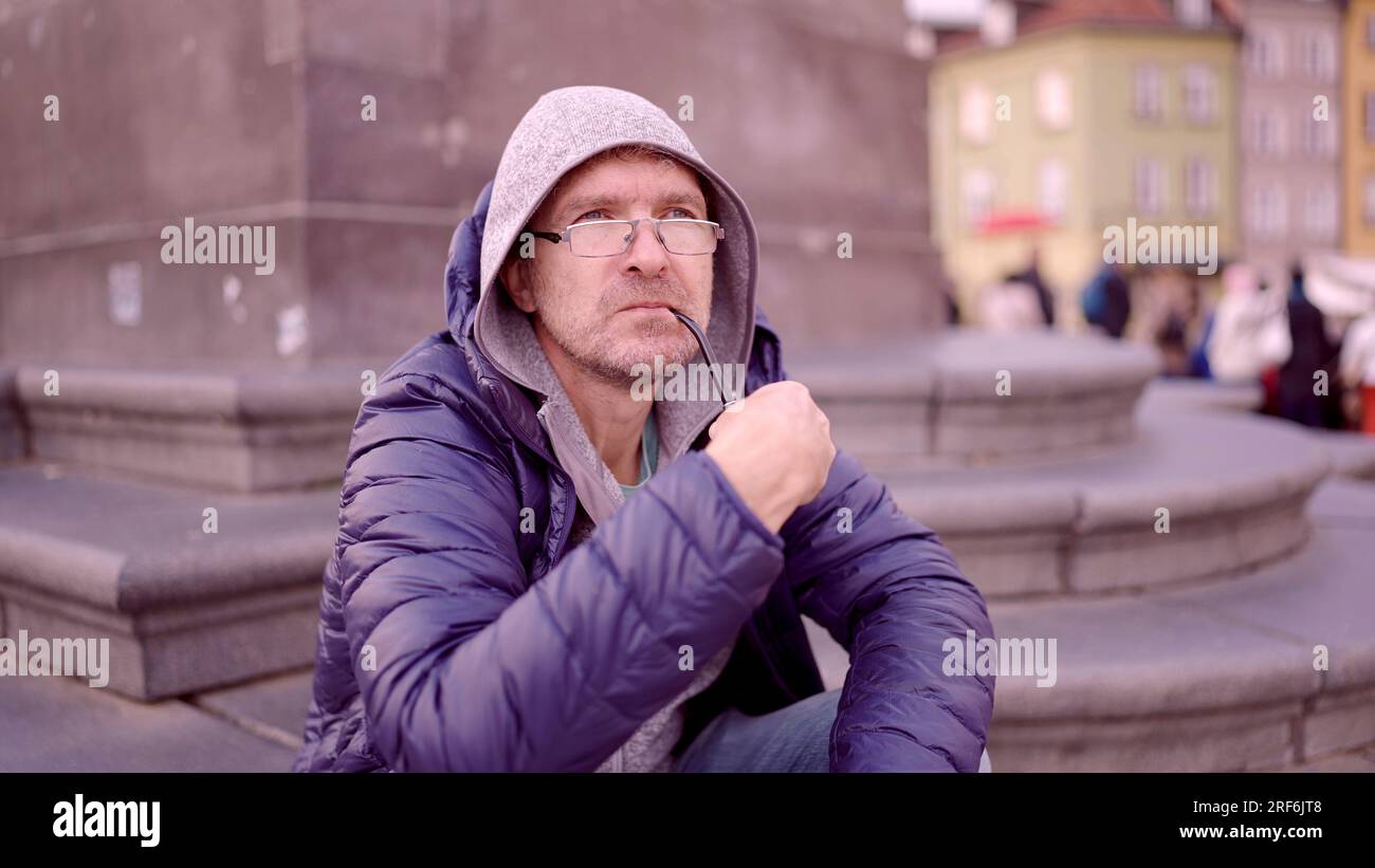 Ritratto di un uomo adulto con occhiali seduti nel cappuccio sulla piazza e fumare un tubo di tabacco nella Piazza del Palazzo, nella Città Vecchia di Varsavia Foto Stock