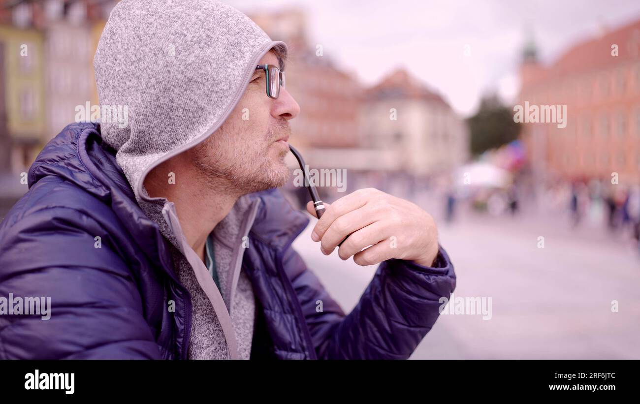 Ritratto di un uomo adulto con occhiali seduti nel cappuccio sulla piazza e fumare un tubo di tabacco nella Piazza del Palazzo, nella Città Vecchia di Varsavia Foto Stock