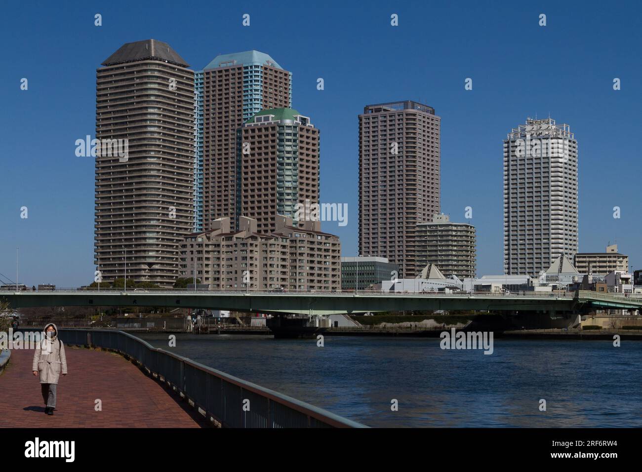 Una donna lungo il fiume Sumida con alti edifici di appartamenti dietro. Tokyo, Giappone. Foto Stock
