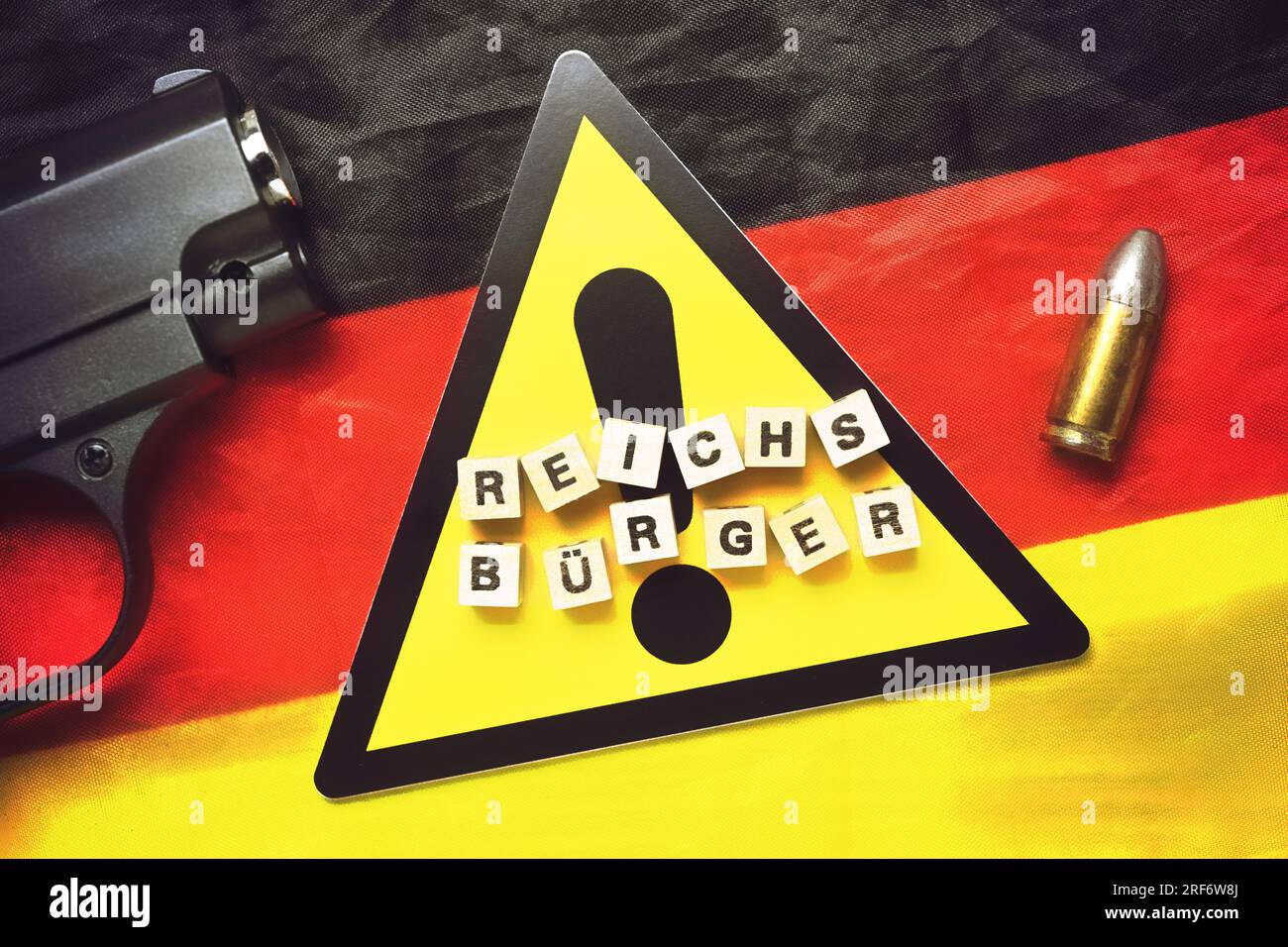 Buchstabenwürfel formen das Wort Reichsbürger auf Gefahrenschild und Deutschlandfahne Foto Stock