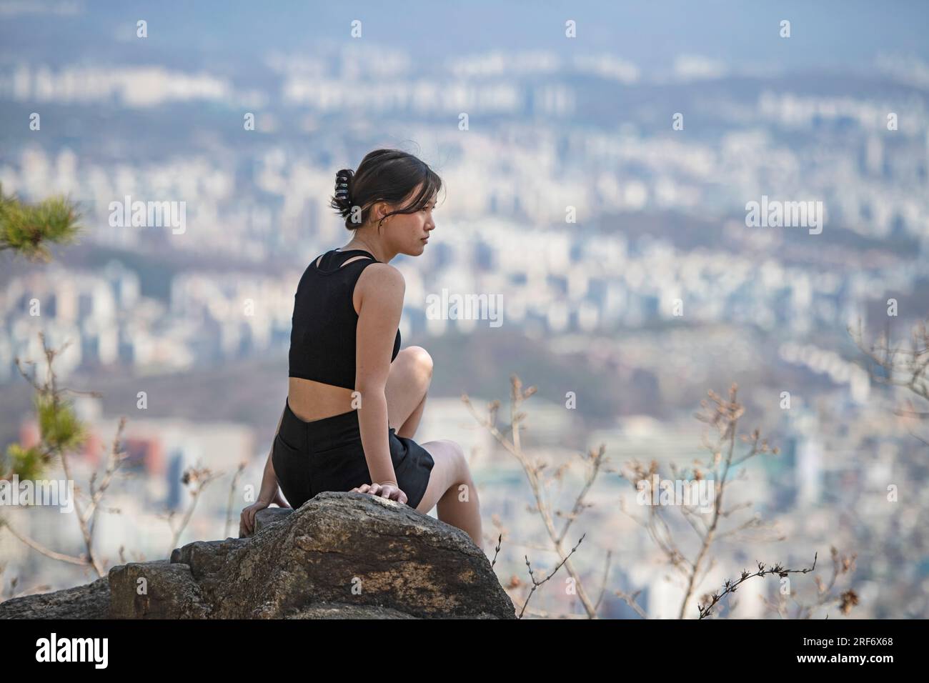 Giovane donna seduta sulla roccia a Buk Han san, catena montuosa a nord di Seul, con vista su Seul Foto Stock