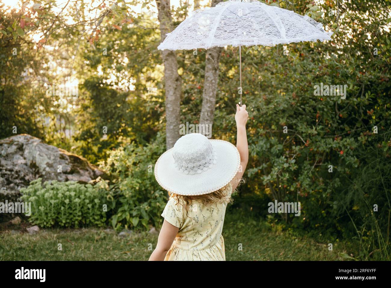 La bambina tiene in mano un ombrellone bianco in pizzo in una bella serata di sole nella natura. Concetto di aspirazioni da sogno. Foto Stock