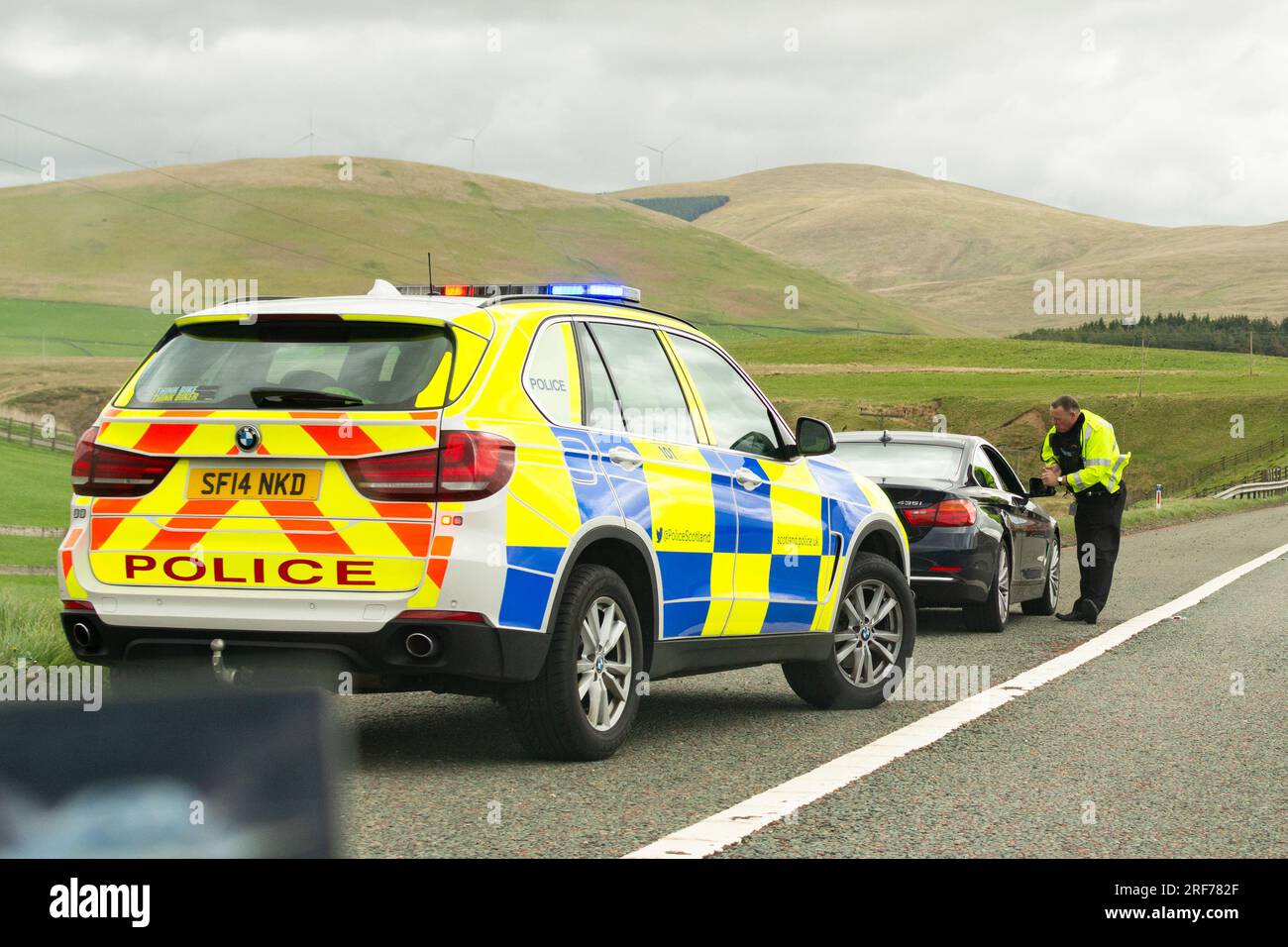 Agente della polizia stradale che parla al conducente di una bmw nera che è stata fatta per accostare sulla spalla rigida dell'autostrada M74 Scozia, Regno Unito Foto Stock