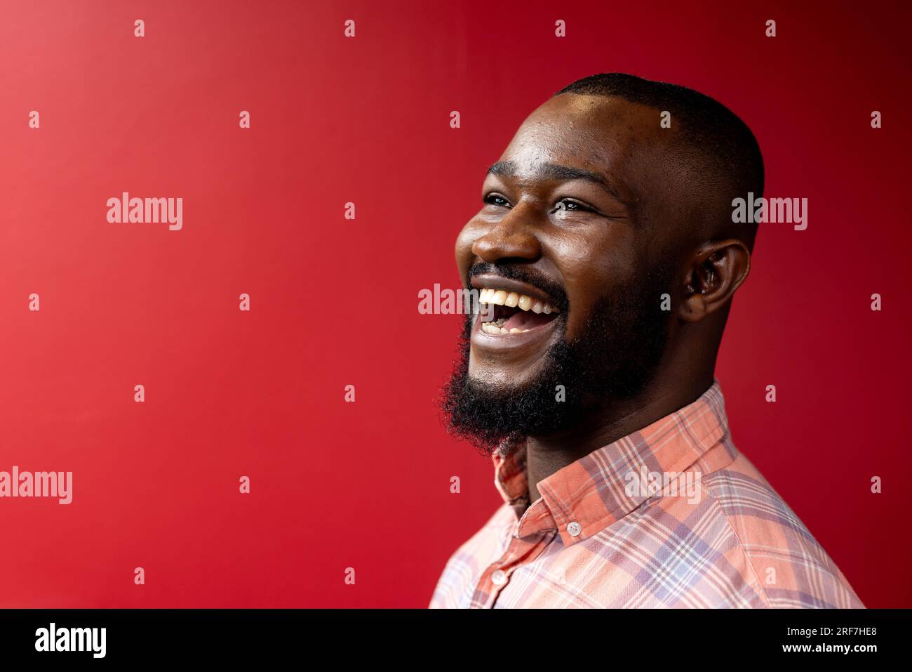 Vista laterale di un uomo d'affari afroamericano sorridente su sfondo rosso, spazio copia Foto Stock