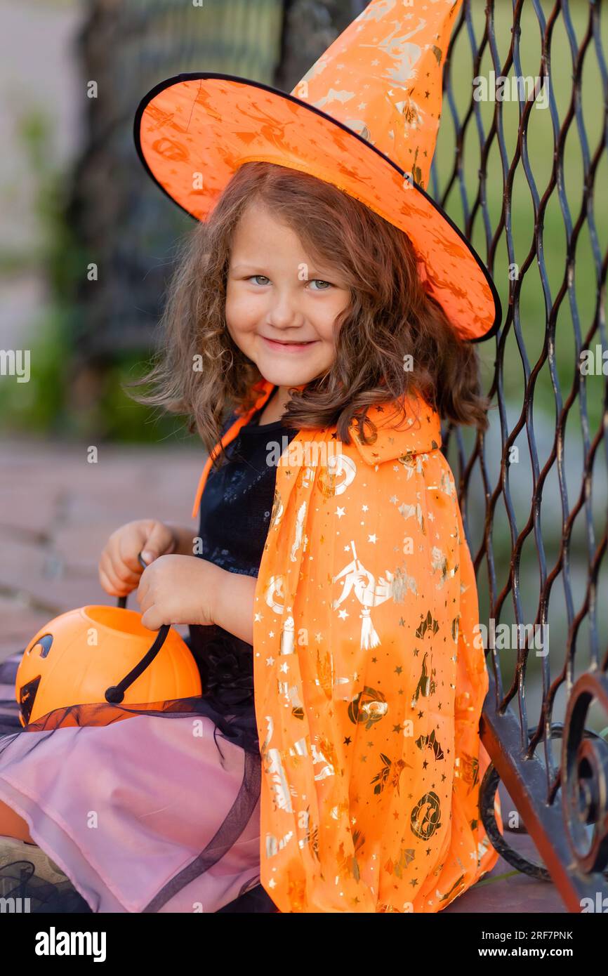 Una graziosa bambina in costume da strega per Halloween cammina nel parco in un cesto di caramelle a forma di zucca. Foto di alta qualità Foto Stock