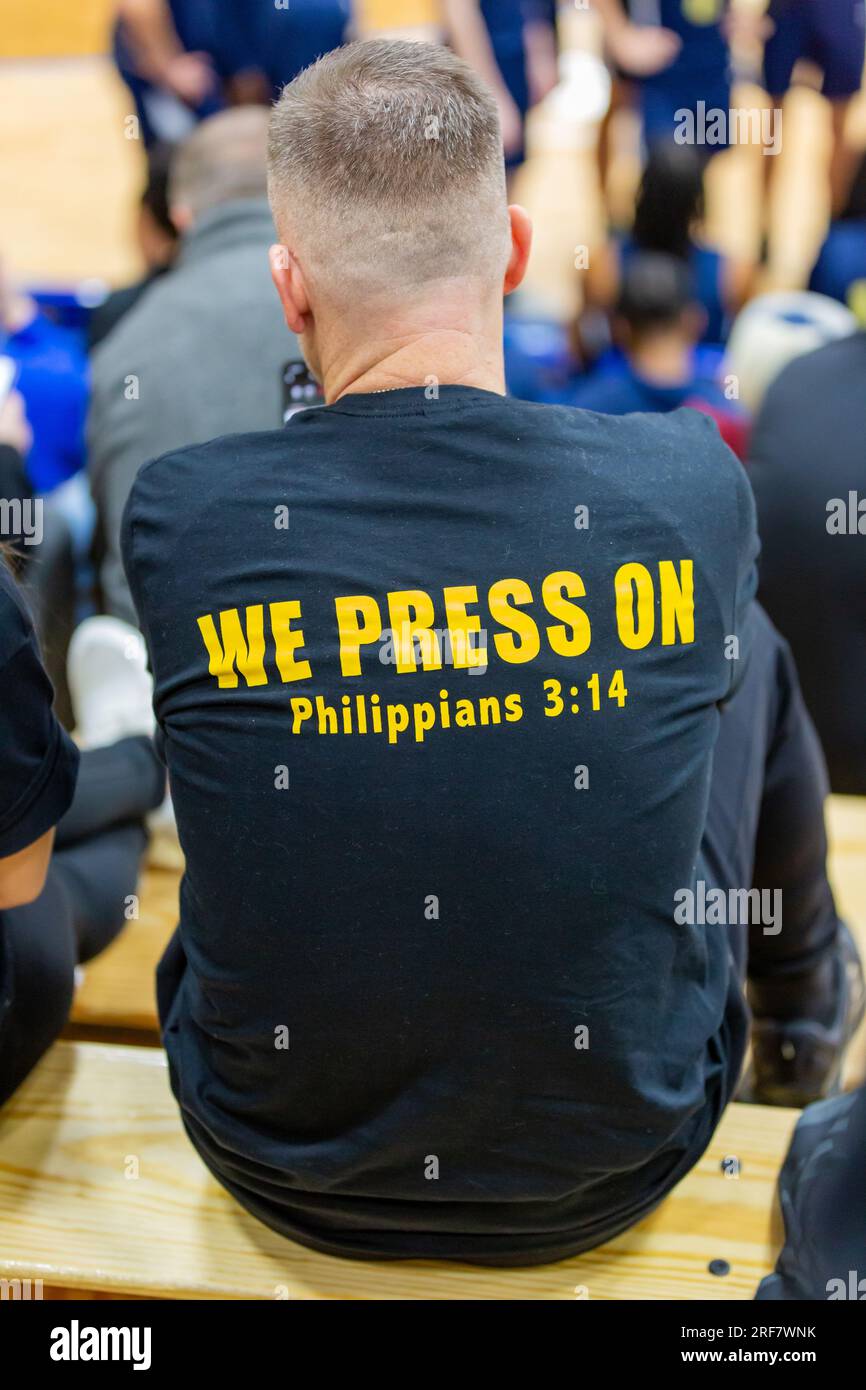 Un uomo con un versetto della Bibbia stampato sul retro della sua maglietta siede nei gradini durante un evento. Foto Stock