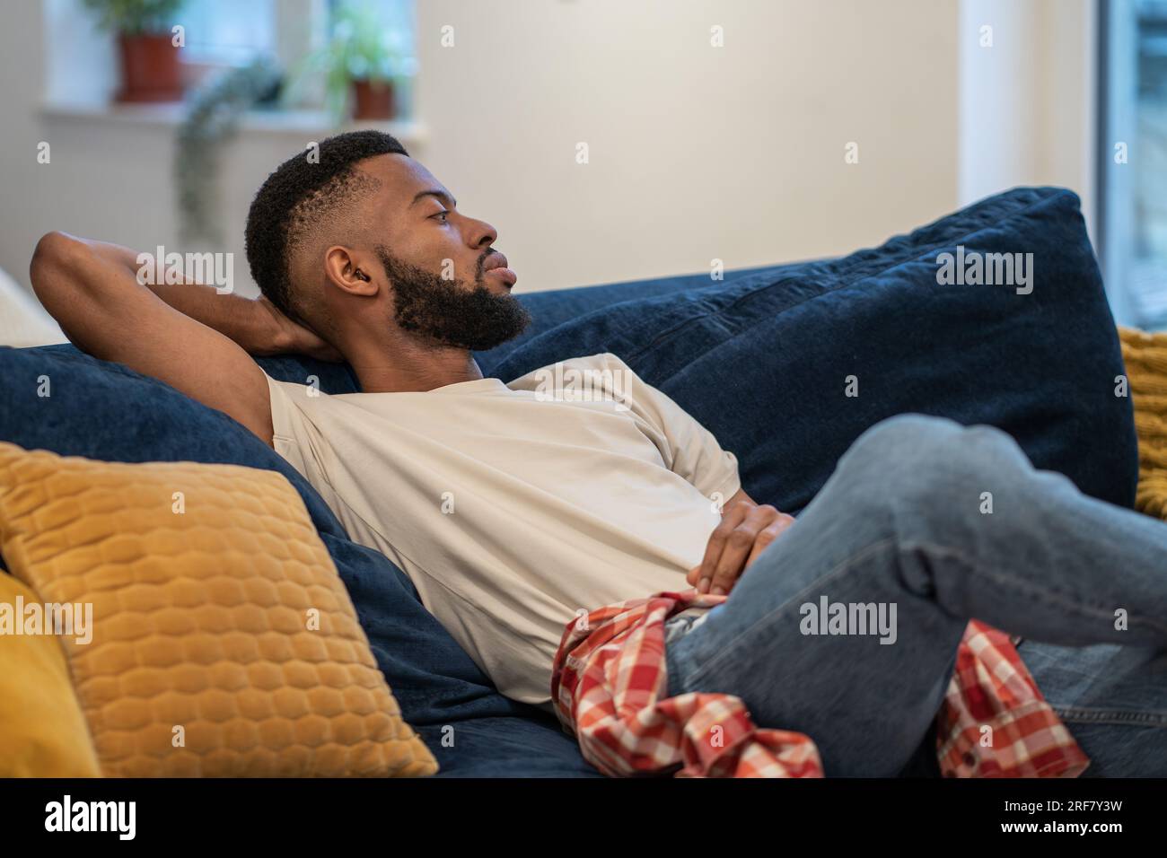 Il ragazzo afro-americano sognante e premuroso siede su divani appoggiati nel monolocale. Foto Stock