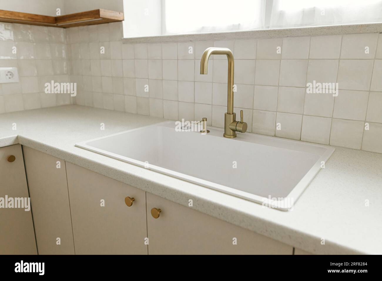 Cucina dal design moderno e minimalista. Elegante rubinetto in ottone e lavandino in granito bianco, armadi da cucina con pomelli e bancone in granito nella nuova casa scandinava. Foto Stock