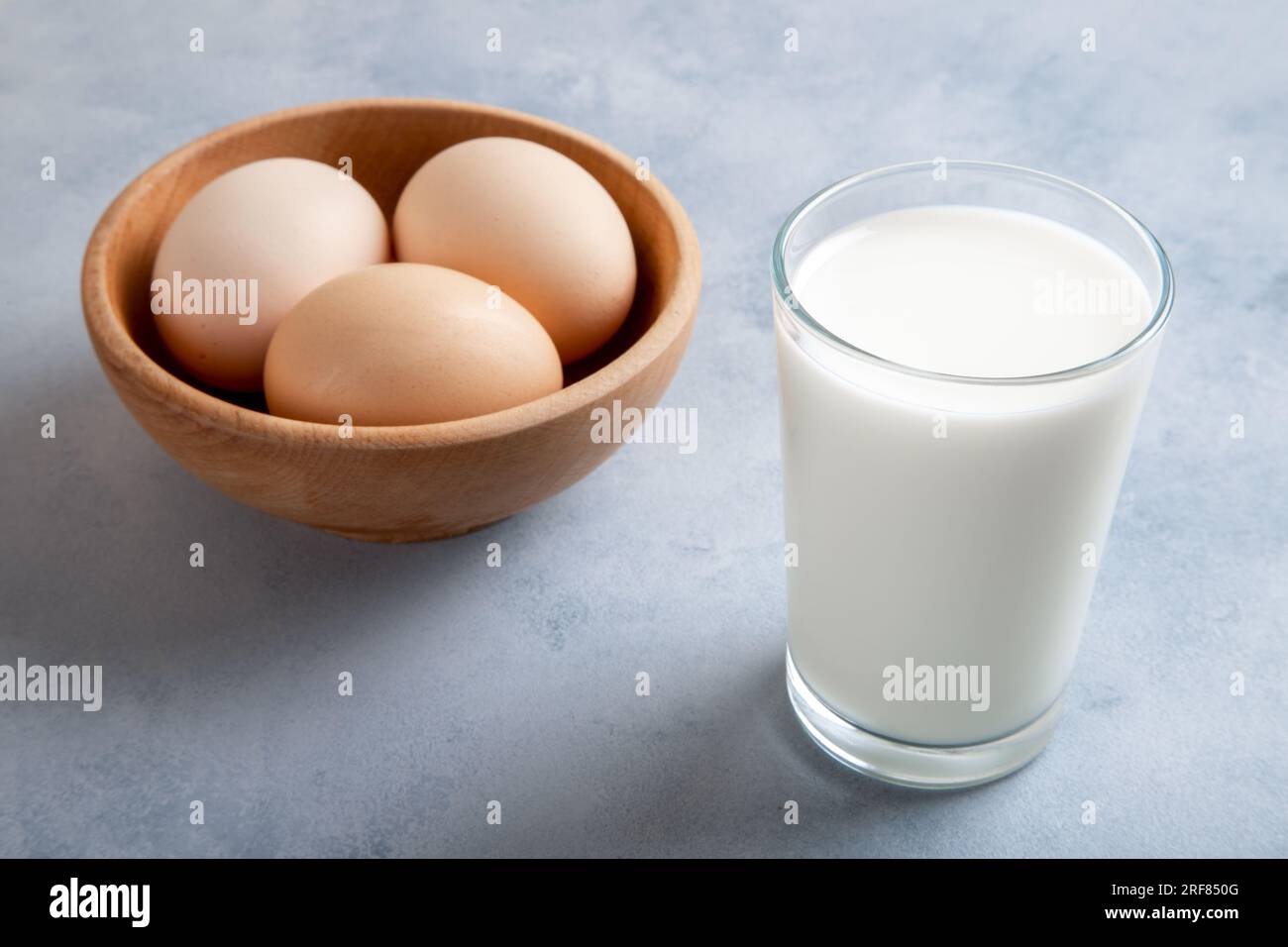 Un bicchiere di latte su sfondo blu e uova in una ciotola, vista dall'alto Foto Stock