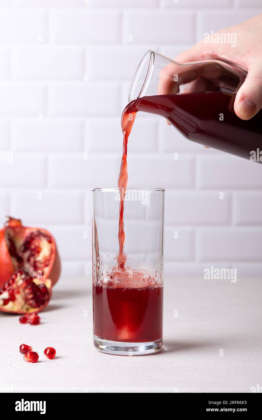 Un uomo versa succo di melograno da una bottiglia in un bicchiere alto con ghiaccio, il concetto di freschezza e utilità. Sullo sfondo, i frutti e le sementi Foto Stock