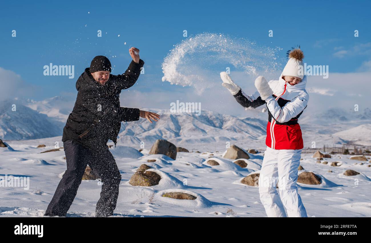 Giovane uomo e donna che giocano a palla di neve sullo sfondo delle montagne nella stagione invernale Foto Stock