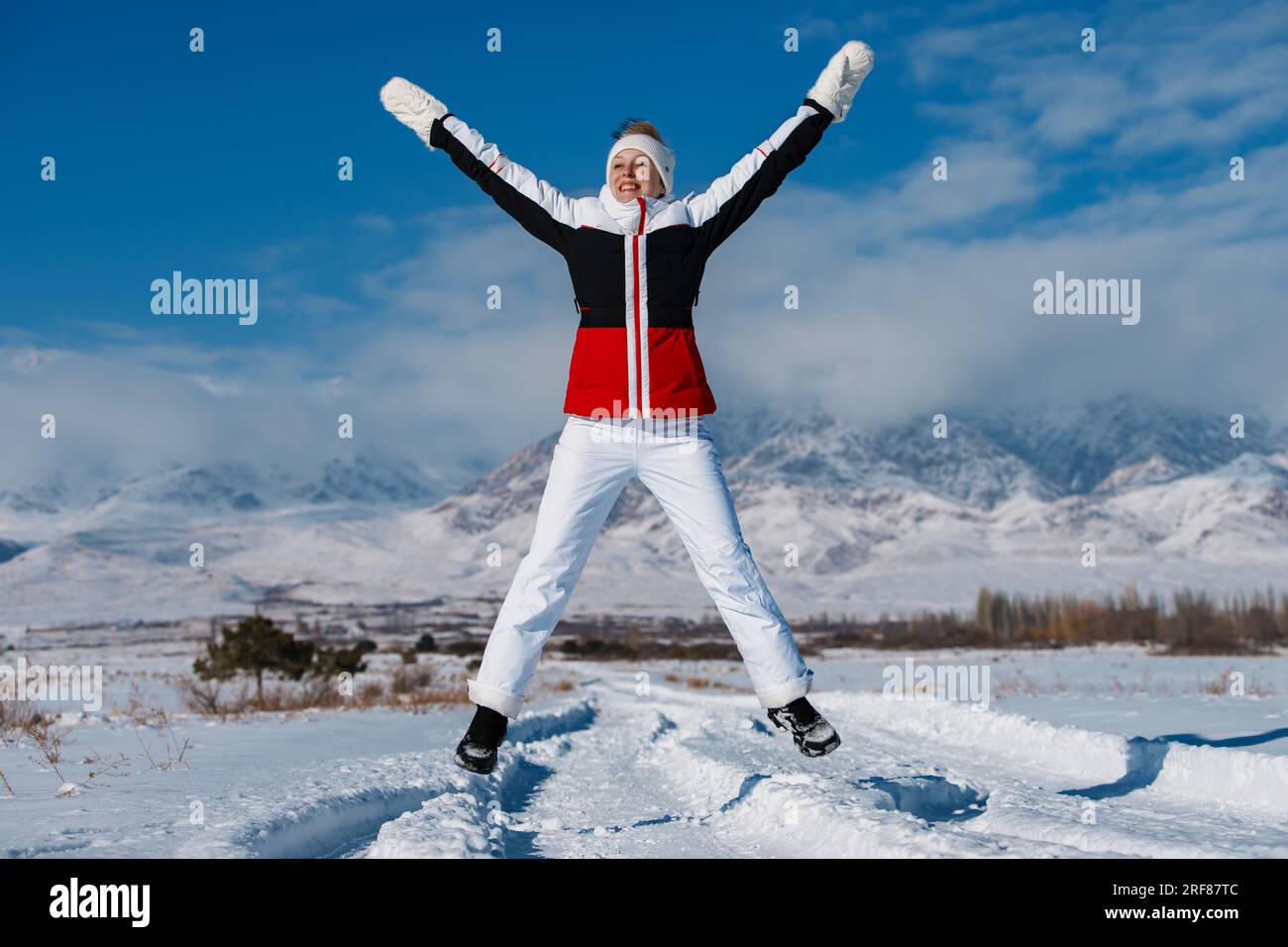 Giovane donna felice che salta sullo sfondo delle montagne nella stagione invernale Foto Stock