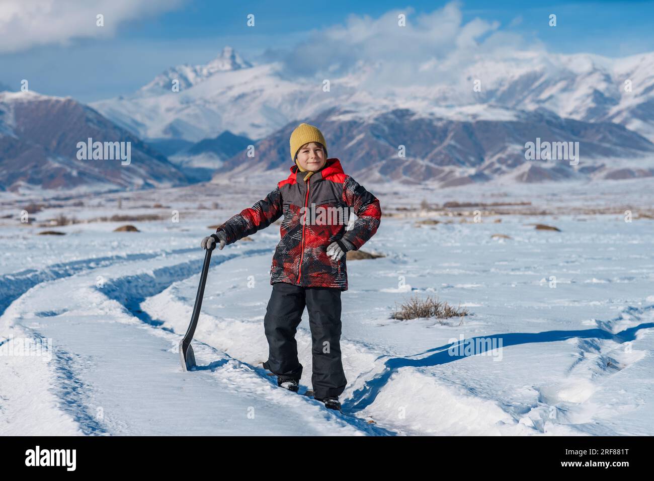 Bambino con pala in piedi sullo sfondo delle montagne invernali Foto Stock