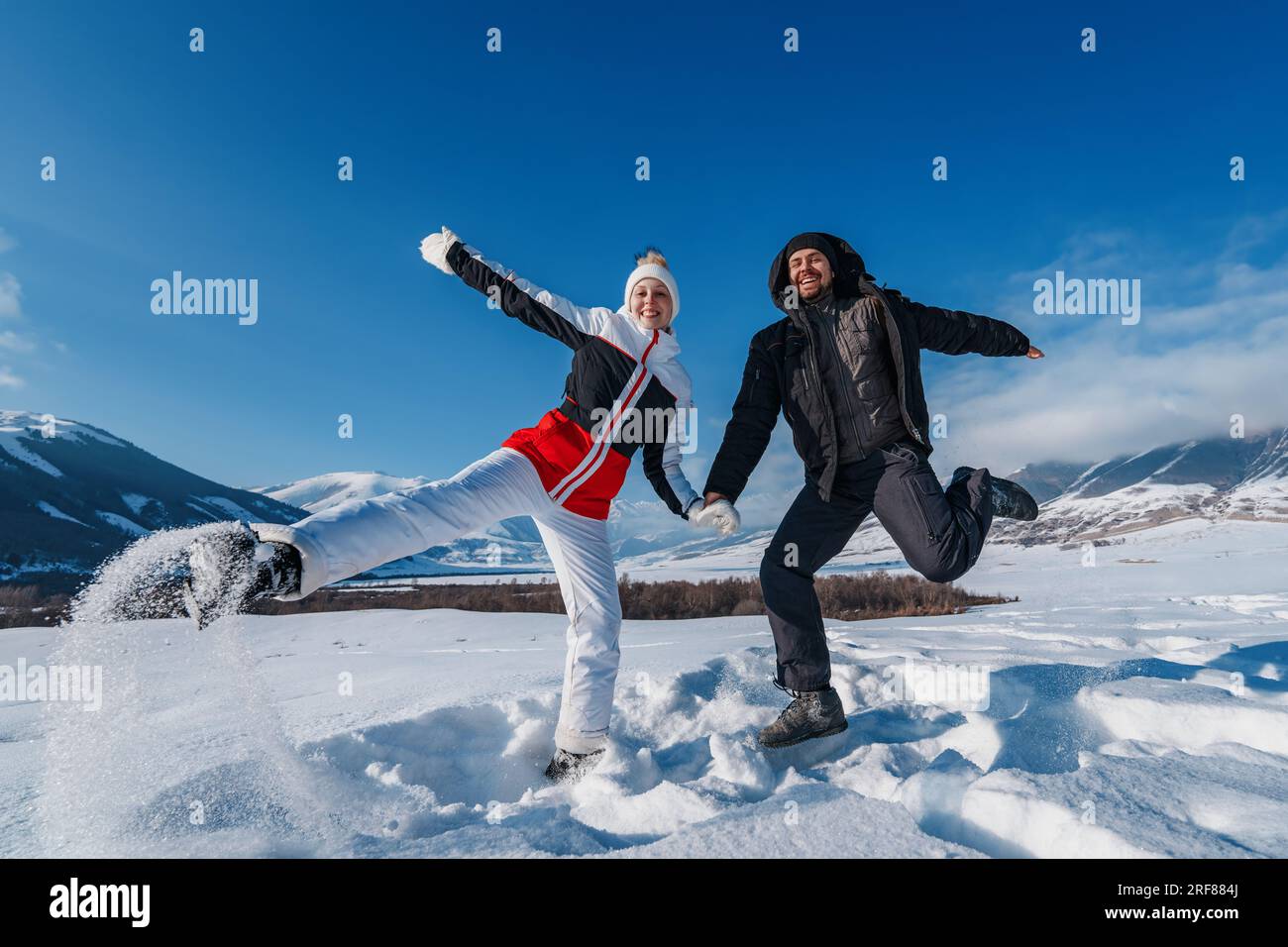 Giovane uomo e donna felici che saltano sullo sfondo delle montagne nella stagione invernale Foto Stock