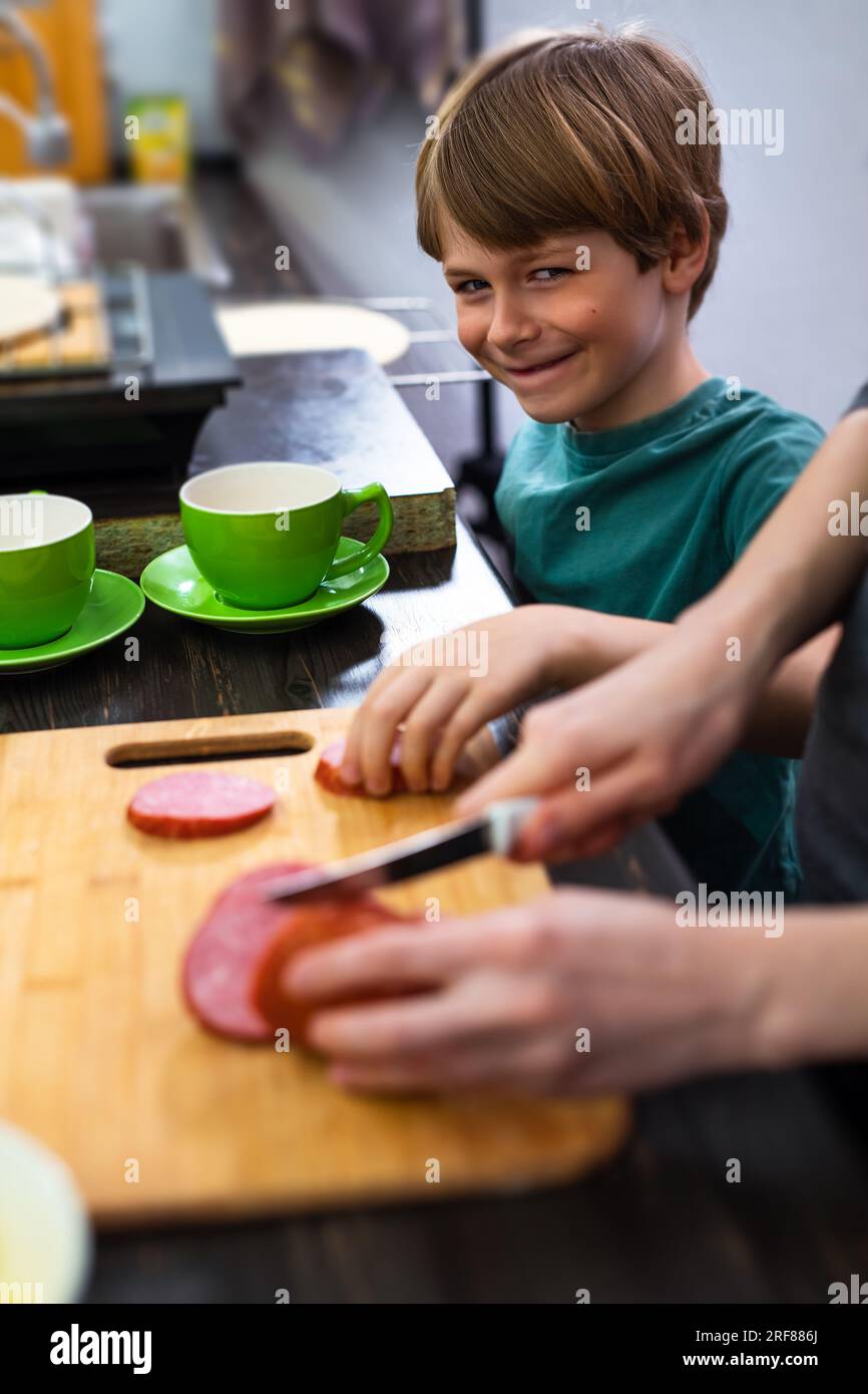 Un bambino intelligente ruba il cibo dal tavolo della cucina quando la madre sta cucinando Foto Stock