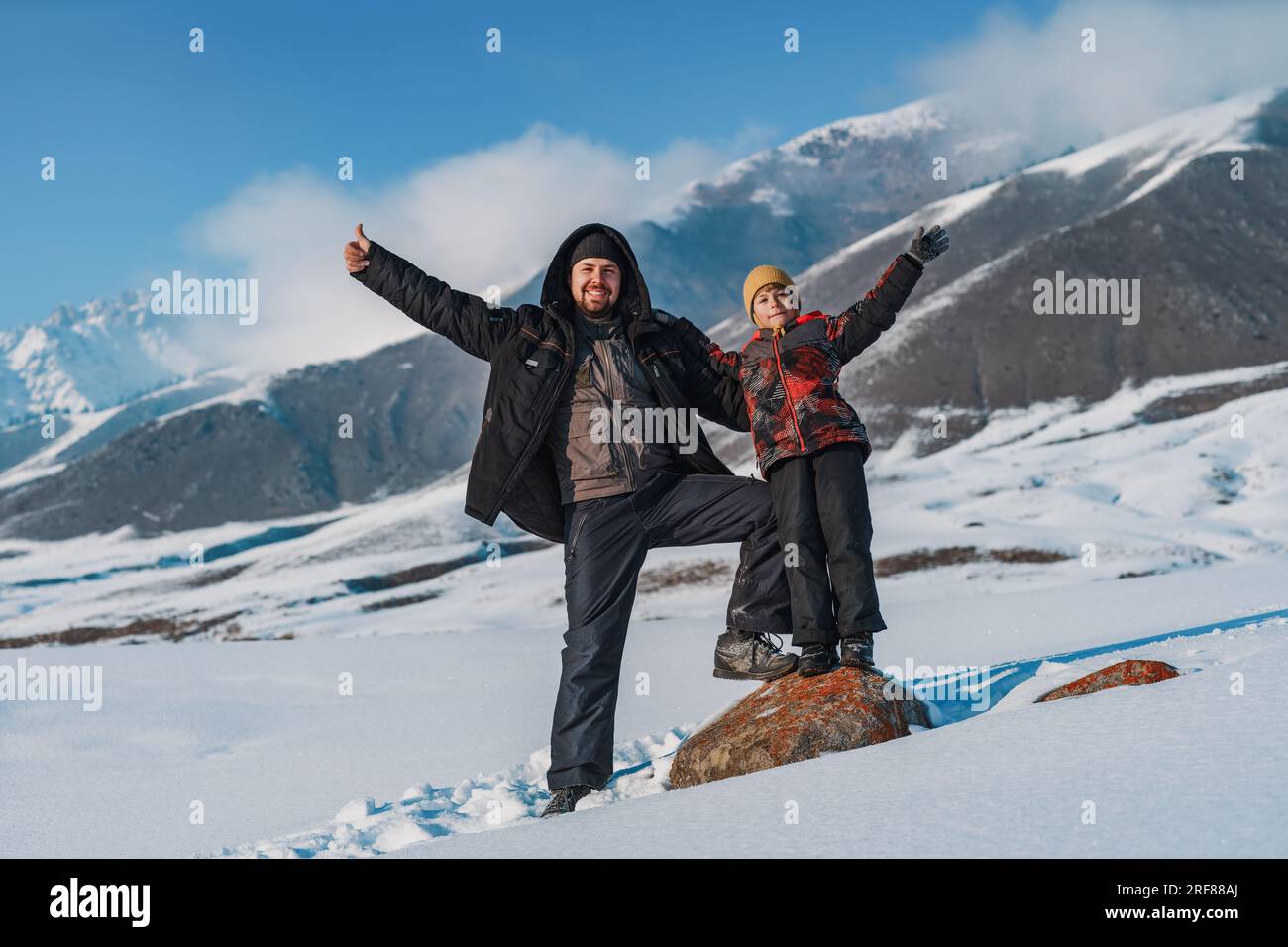 Buon padre e bambino che salutano le mani e si stendono sullo sfondo delle montagne durante la stagione invernale Foto Stock