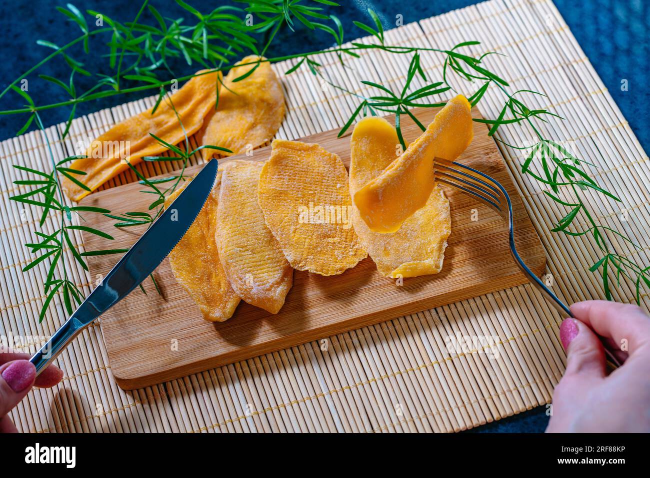 Tavolo da cucina con mango essiccato a bordo, donna che tiene forchetta e coltello Foto Stock