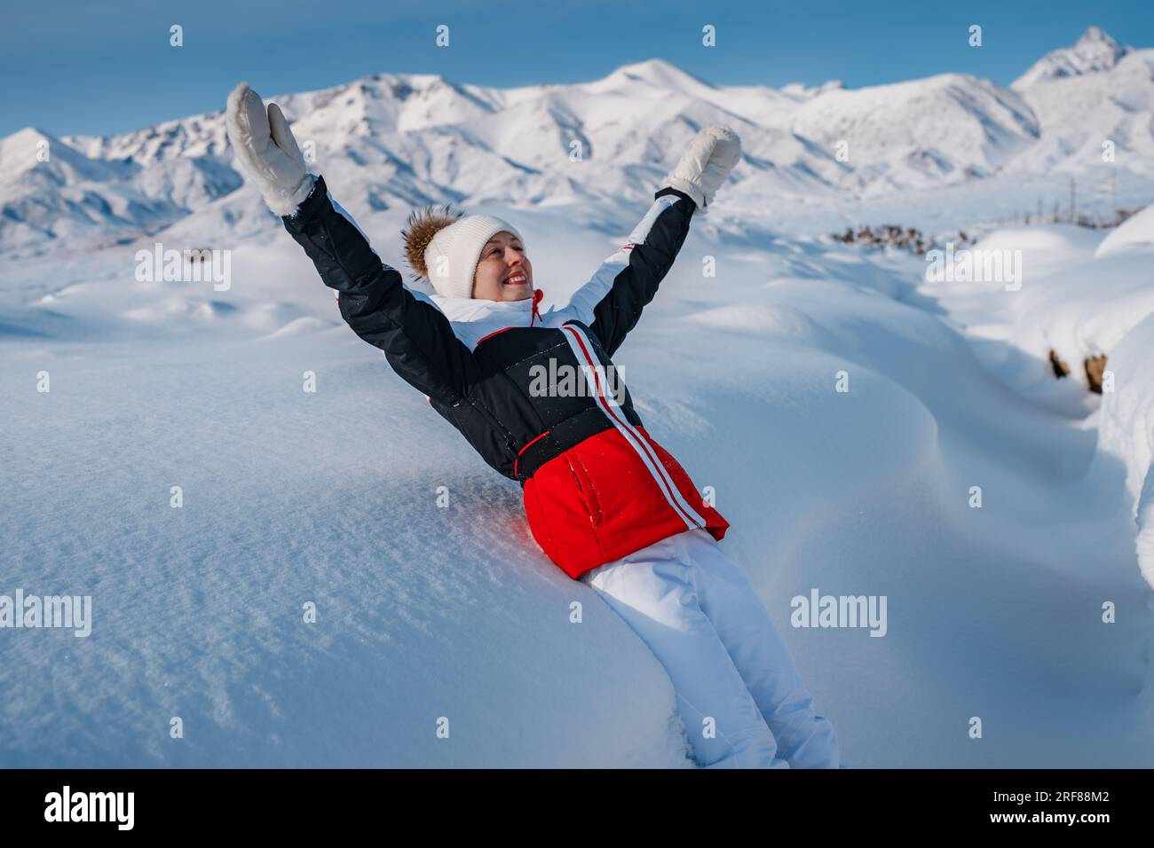Giovane donna turistica allegra che cade nella neve profonda sullo sfondo delle montagne invernali Foto Stock