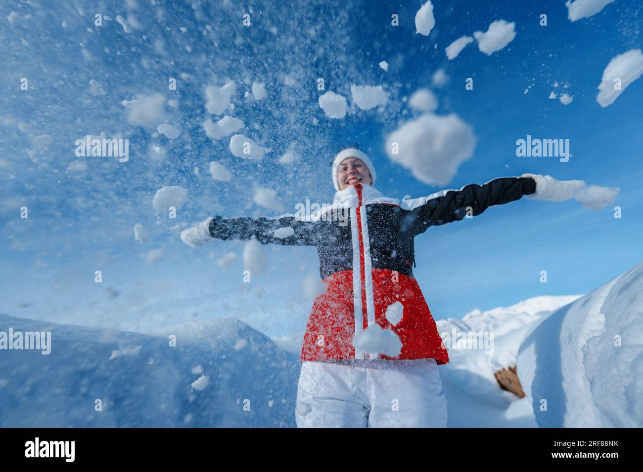 Giovane donna felice lancia la neve sullo sfondo delle montagne invernali Foto Stock