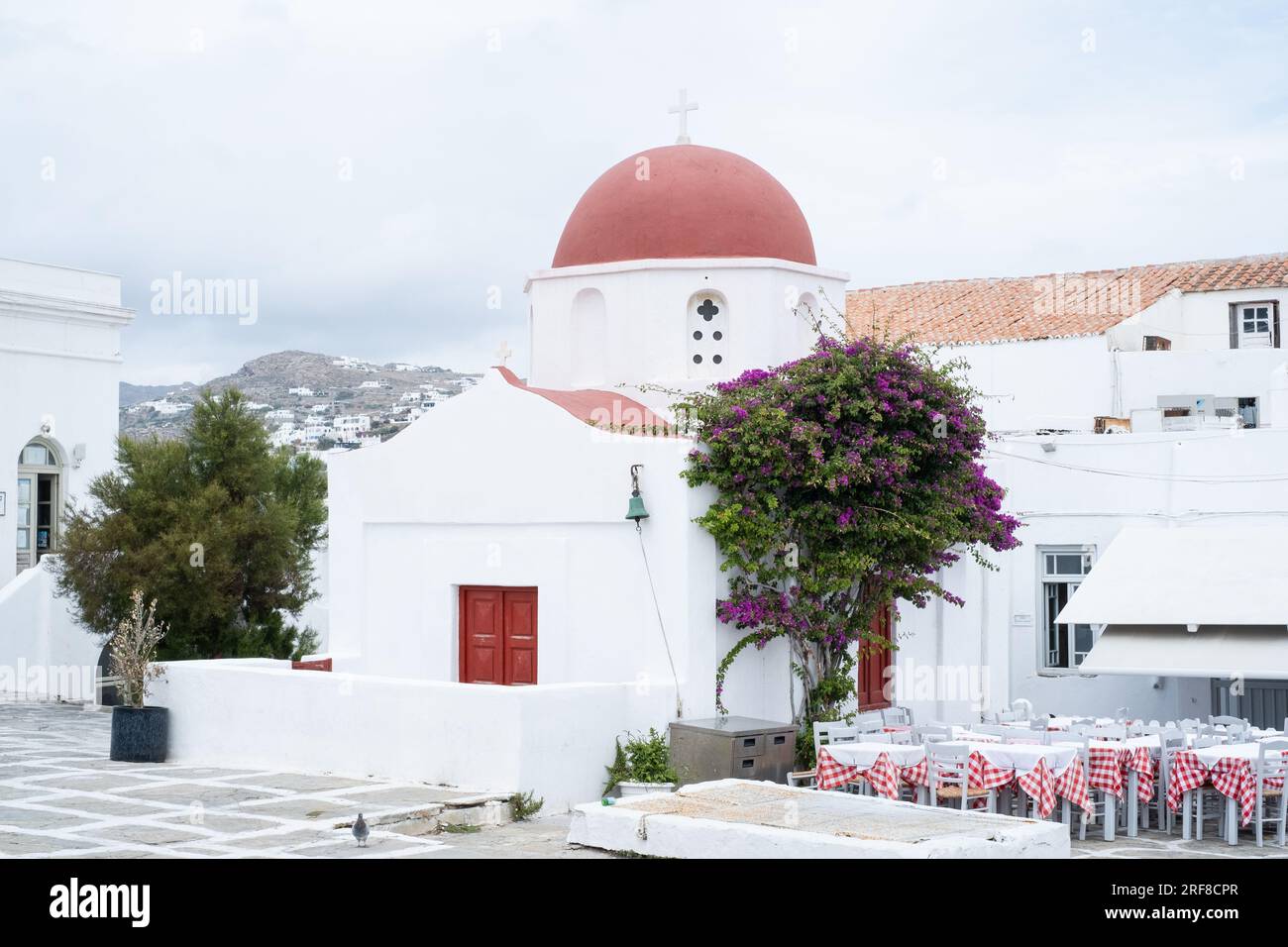 Chiesa con tetto a cupola rosso e tavoli da ristorante sulla destra, Mykonos, Grecia Foto Stock