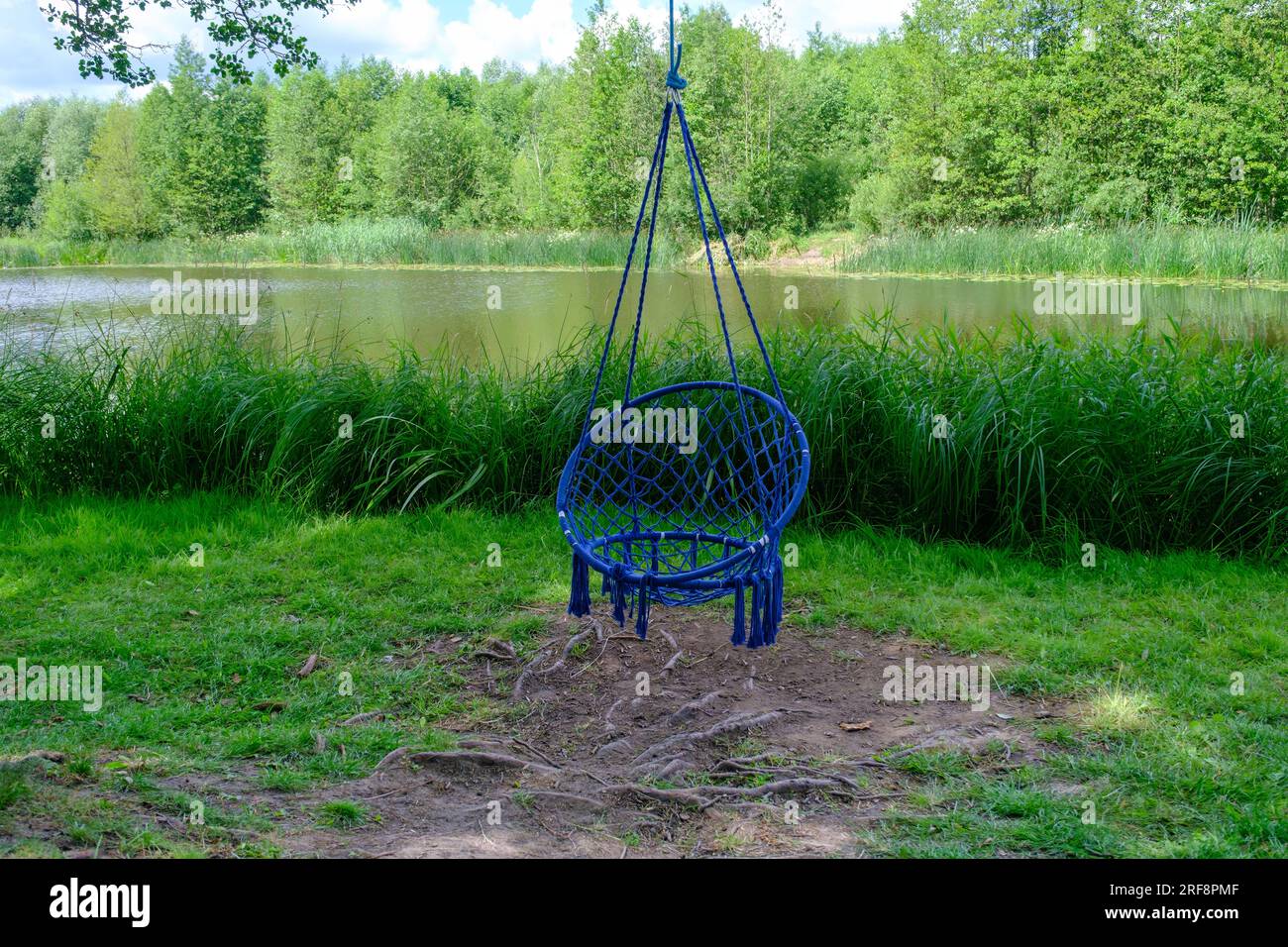Comoda sedia sospesa blu vimini nel giardino estivo. Un accogliente luogo hygge per un fine settimana in giardino. Una sedia di amaca boho appesa su un albero. Supera Foto Stock
